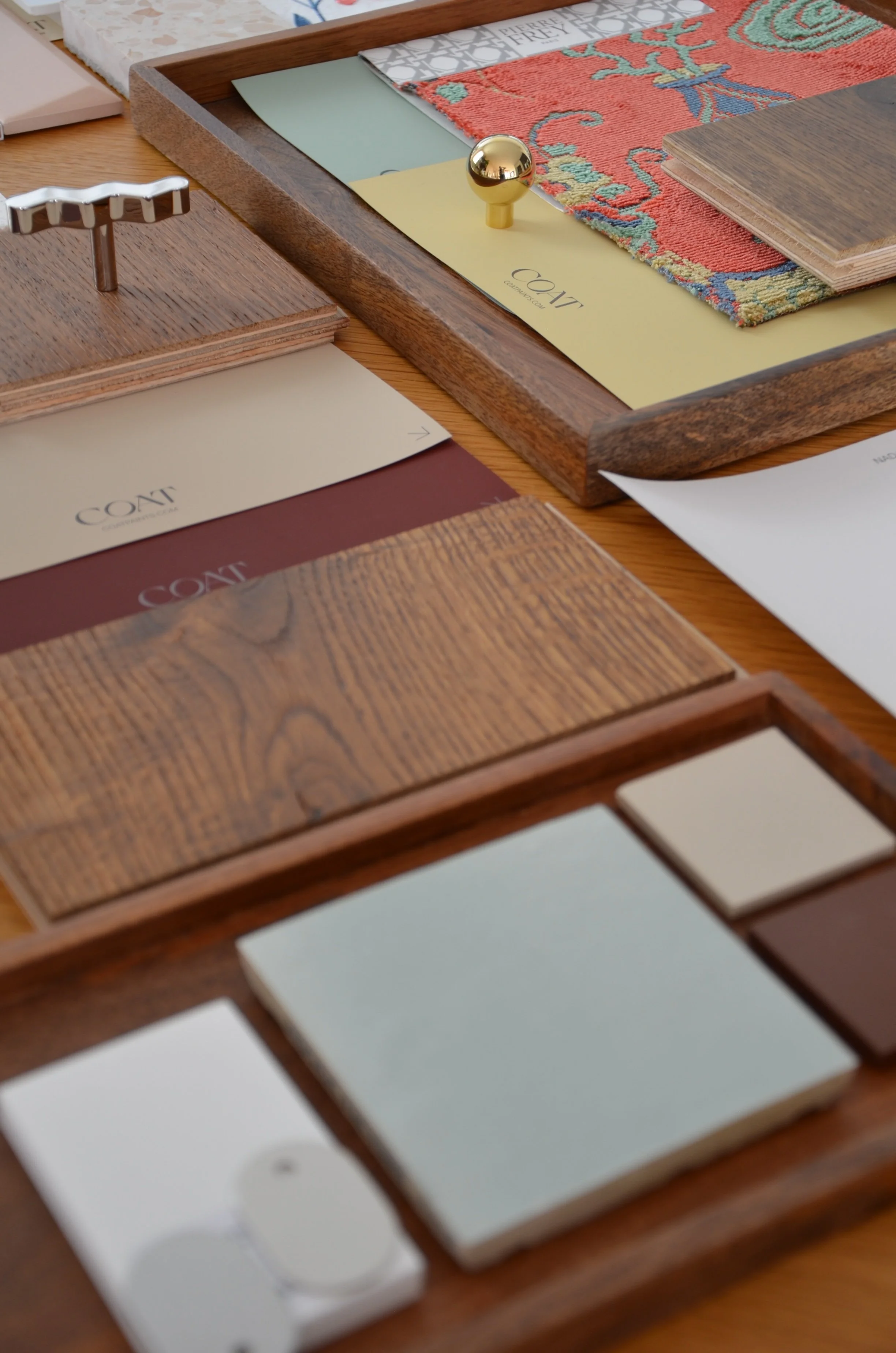 Close-up of a wooden desk or table with design samples, color swatches, and fabric or carpet samples, some labeled 'COT' for color or fabric options.