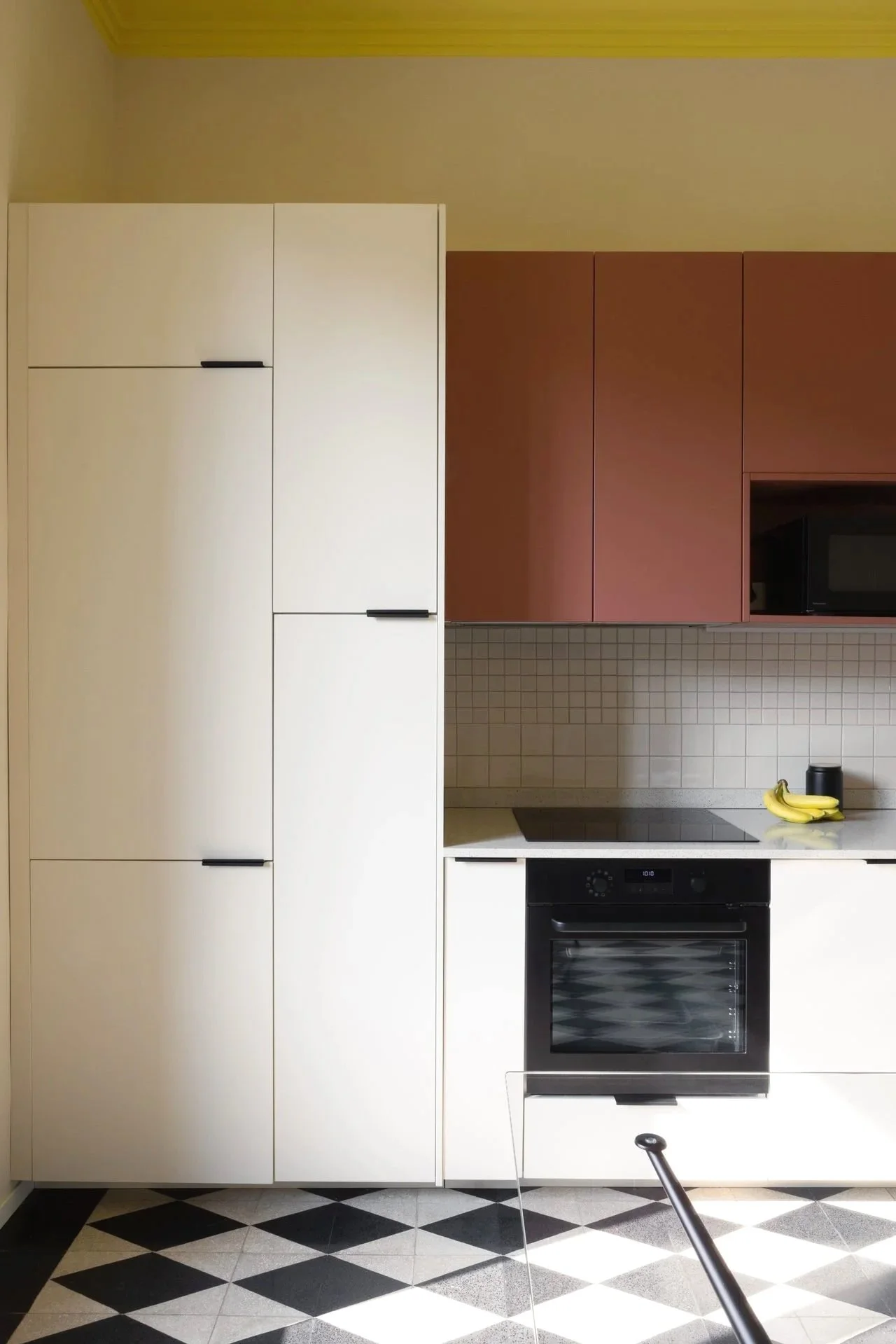 Modern kitchen with white cabinets, red upper cabinets, a black oven, a black microwave, bananas, and a black container on the countertop.
