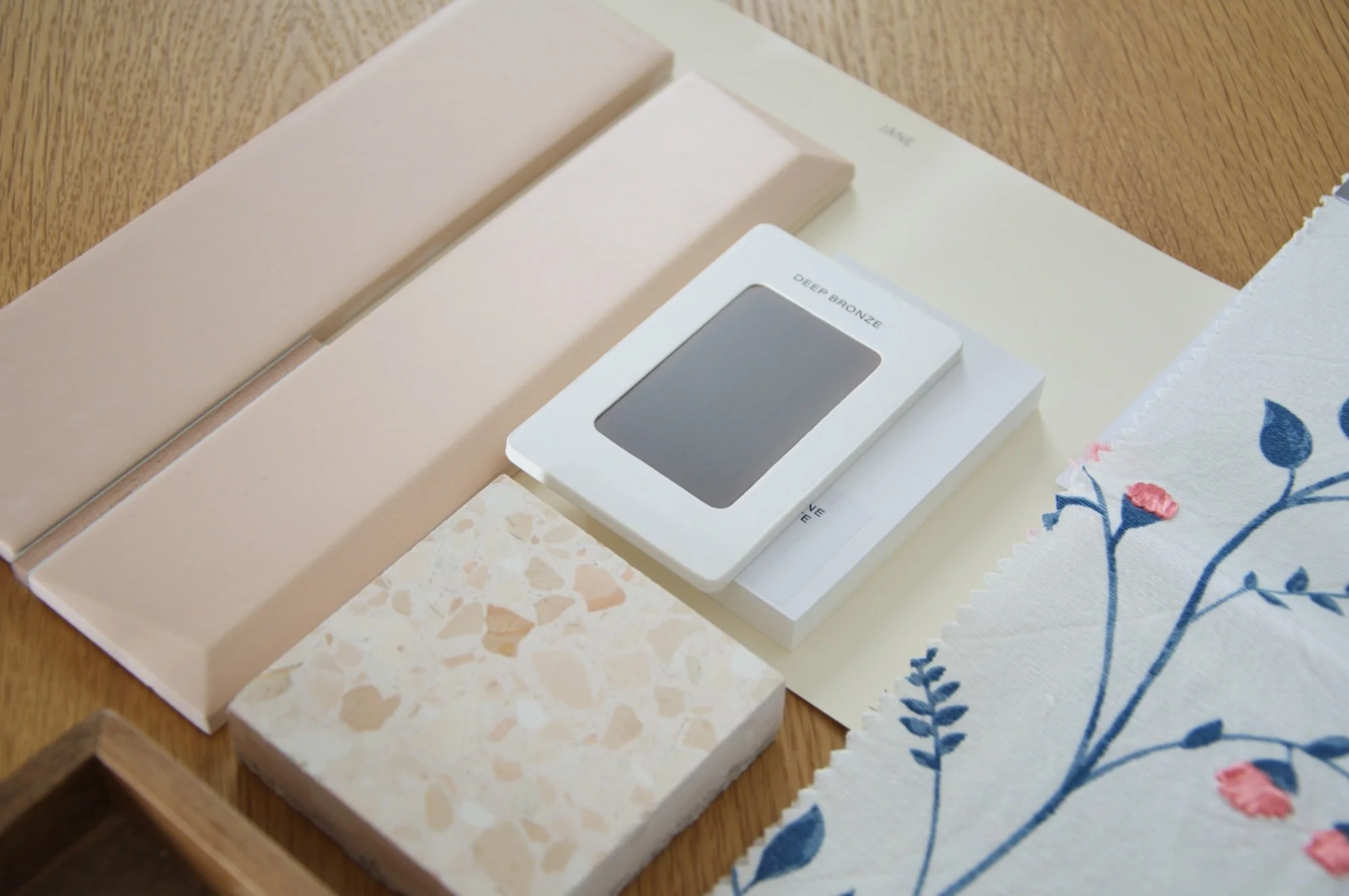 Close-up of a wooden surface with a box containing fabric swatches and color samples, including a Deep Bronze color sample