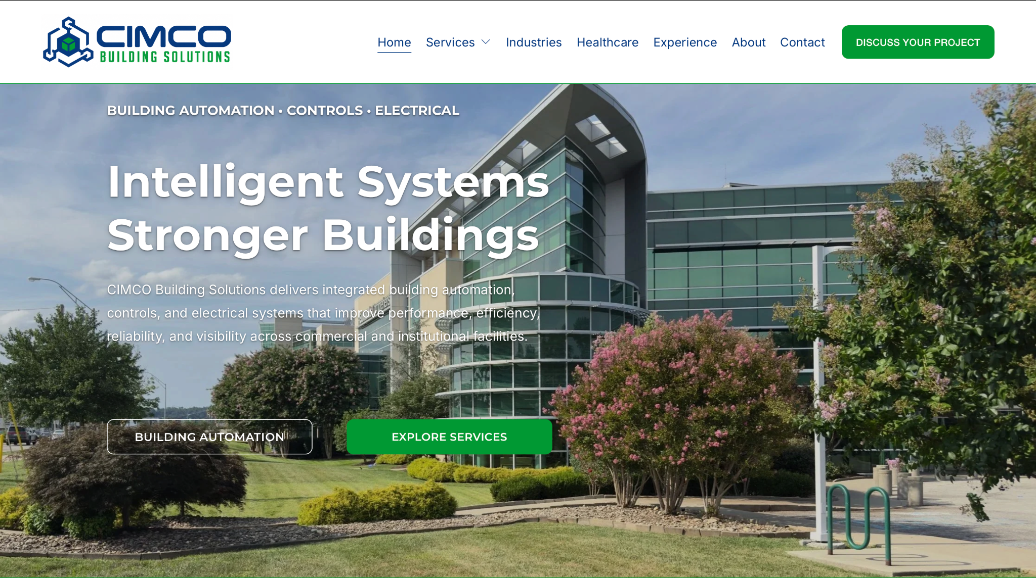 Business website homepage for CIMCO Building Solutions featuring a modern glass building with trees and landscaping in the foreground. The site promotes building automation, controls, and electrical systems.