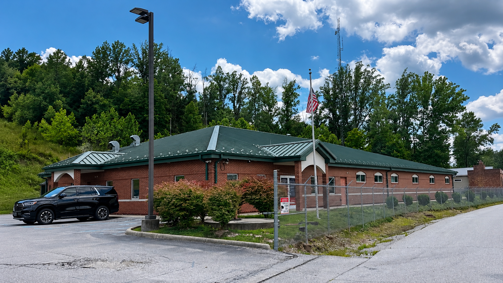 Putnam County 911 and emergency operations building with brick exterior, green metal roof, parking area, flagpole, and rooftop communication antenna.