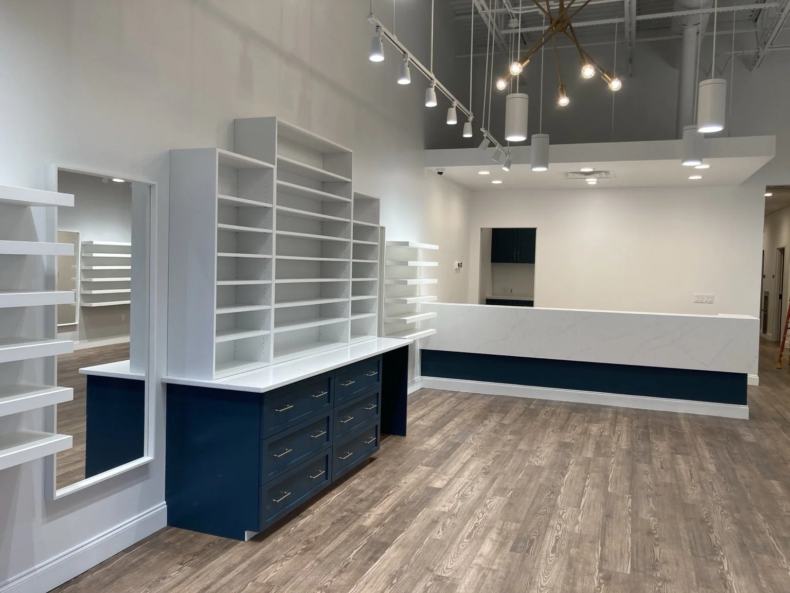 Interior of a retail space with white and navy blue shelving, a reception desk, wood flooring, and modern lighting fixtures.
