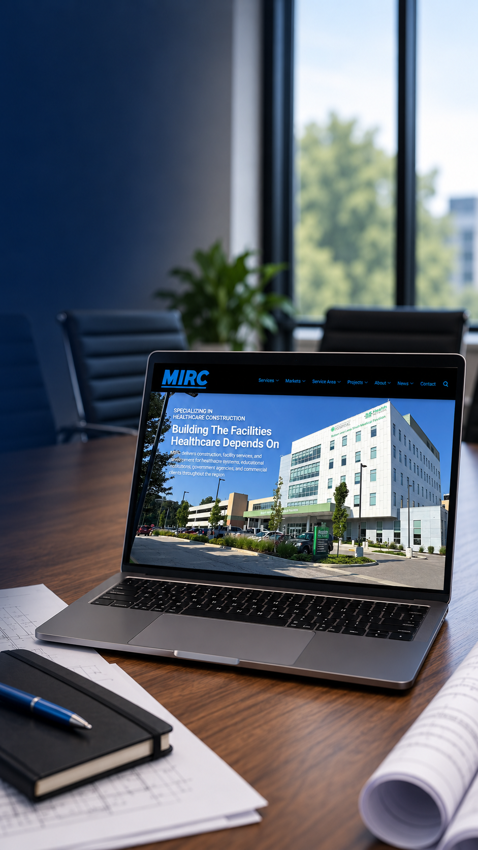 MIRC Construction website displayed on a laptop in a conference room with architectural plans