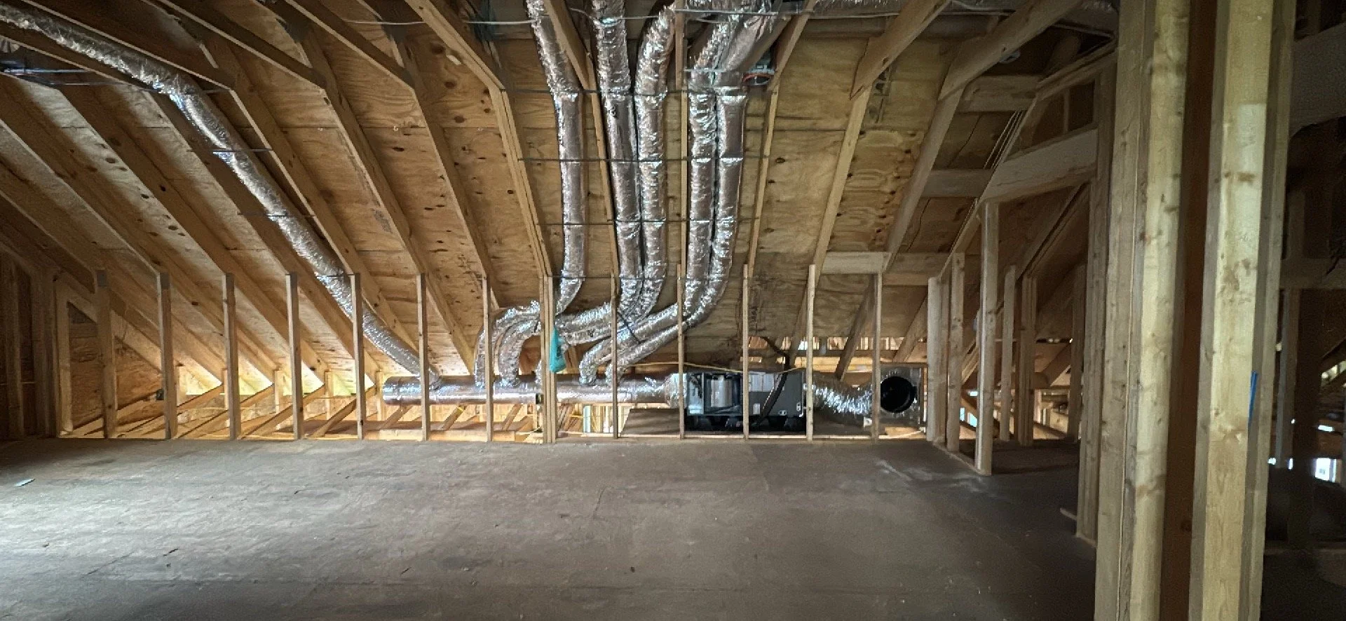 Attic space under construction with exposed wooden framing and HVAC ductwork installed.