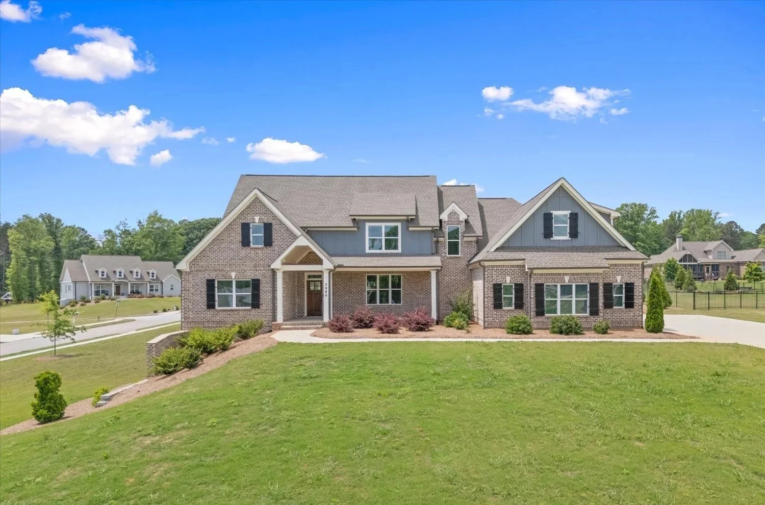 A large modern house with brick and gray siding exterior, multiple gabled roofs, black shutters, and a well-maintained front yard under a clear blue sky.