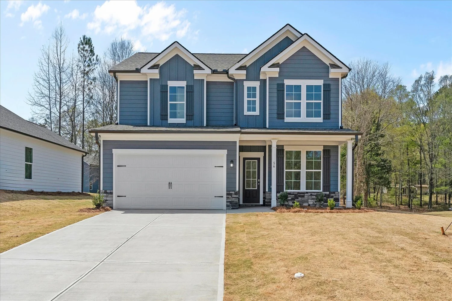 New two-story blue house with white trim and black shutters, attached two-car garage, front porch, and a well-kept lawn in a suburban neighborhood.