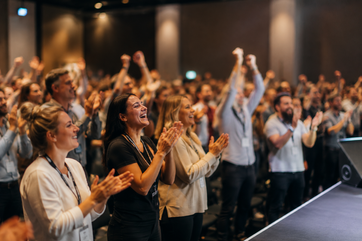 People clapping and cheering at a conference or event in a large indoor venue.