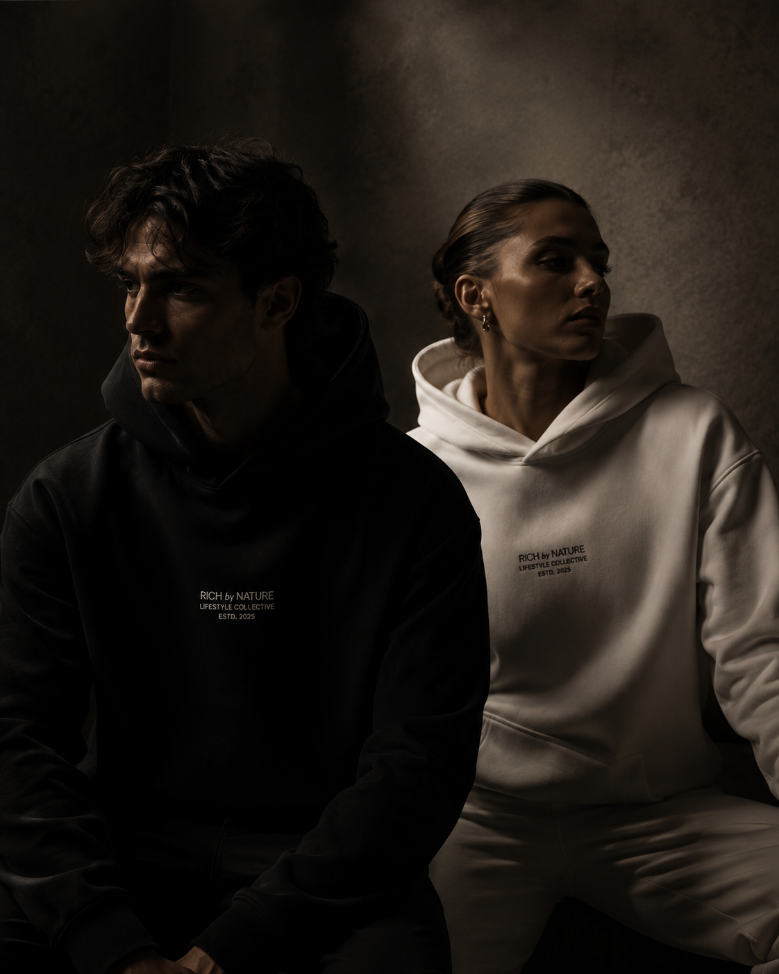 To personer iført sweatshirt, en i svart og en i hvit, sitter side om side mot en mørk bakgrunn, begge ser bort fra hverandre.