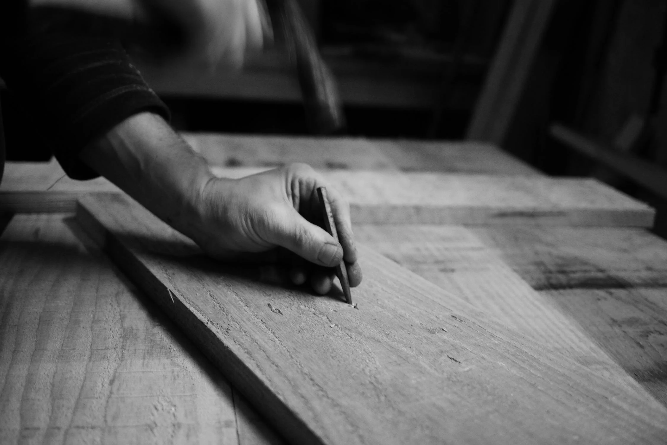 Close-up of a Rufus McIntosh carving or shaping wood with a hand-held tool in a woodworking or carpentry workshop.