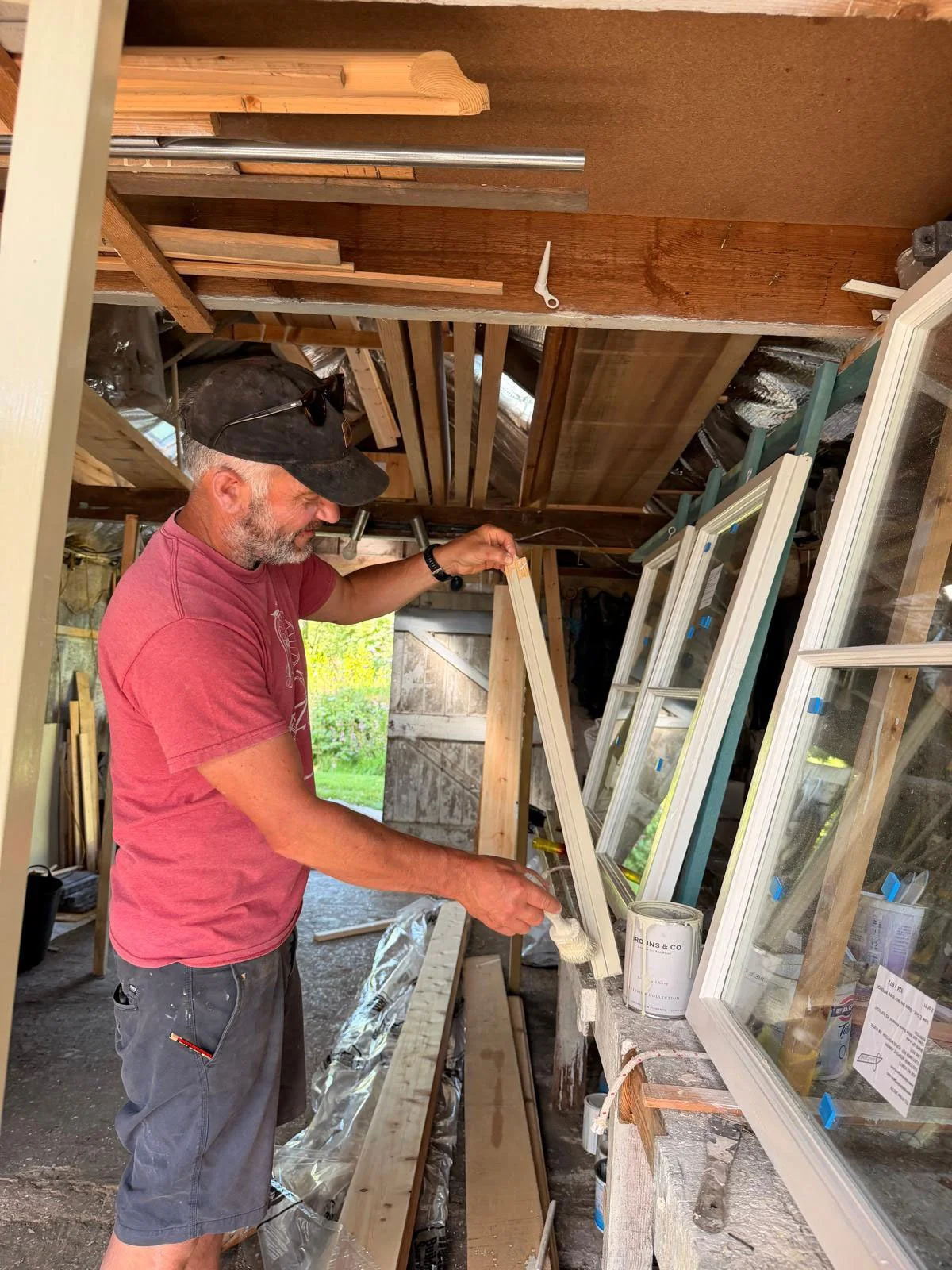 Rufus McIntosh in his woodworking workshop. The workspace has wooden framing, windows, and construction tools visible.