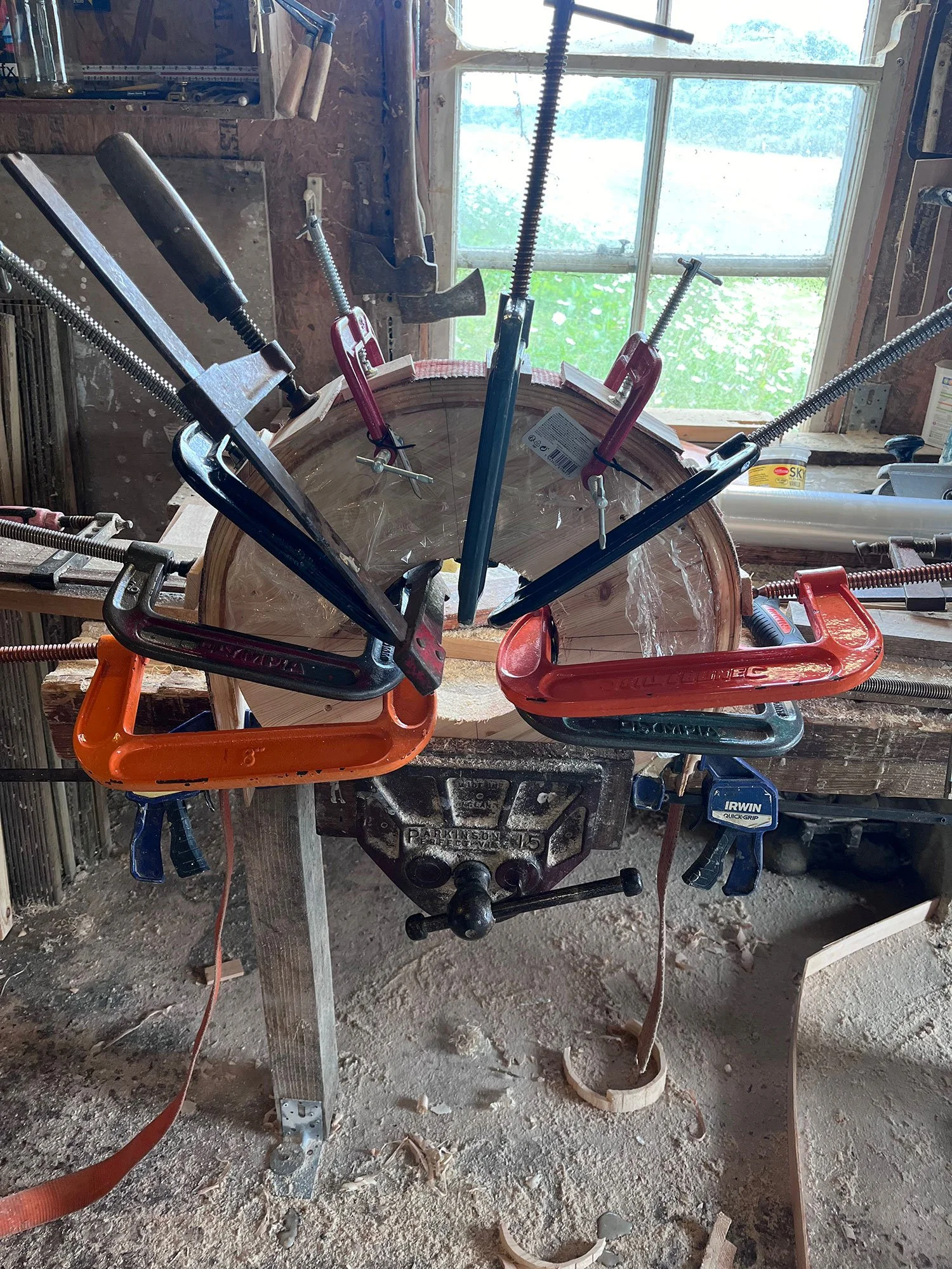Workshop with clamps holding a semicircular piece of wood on a workbench near a window.