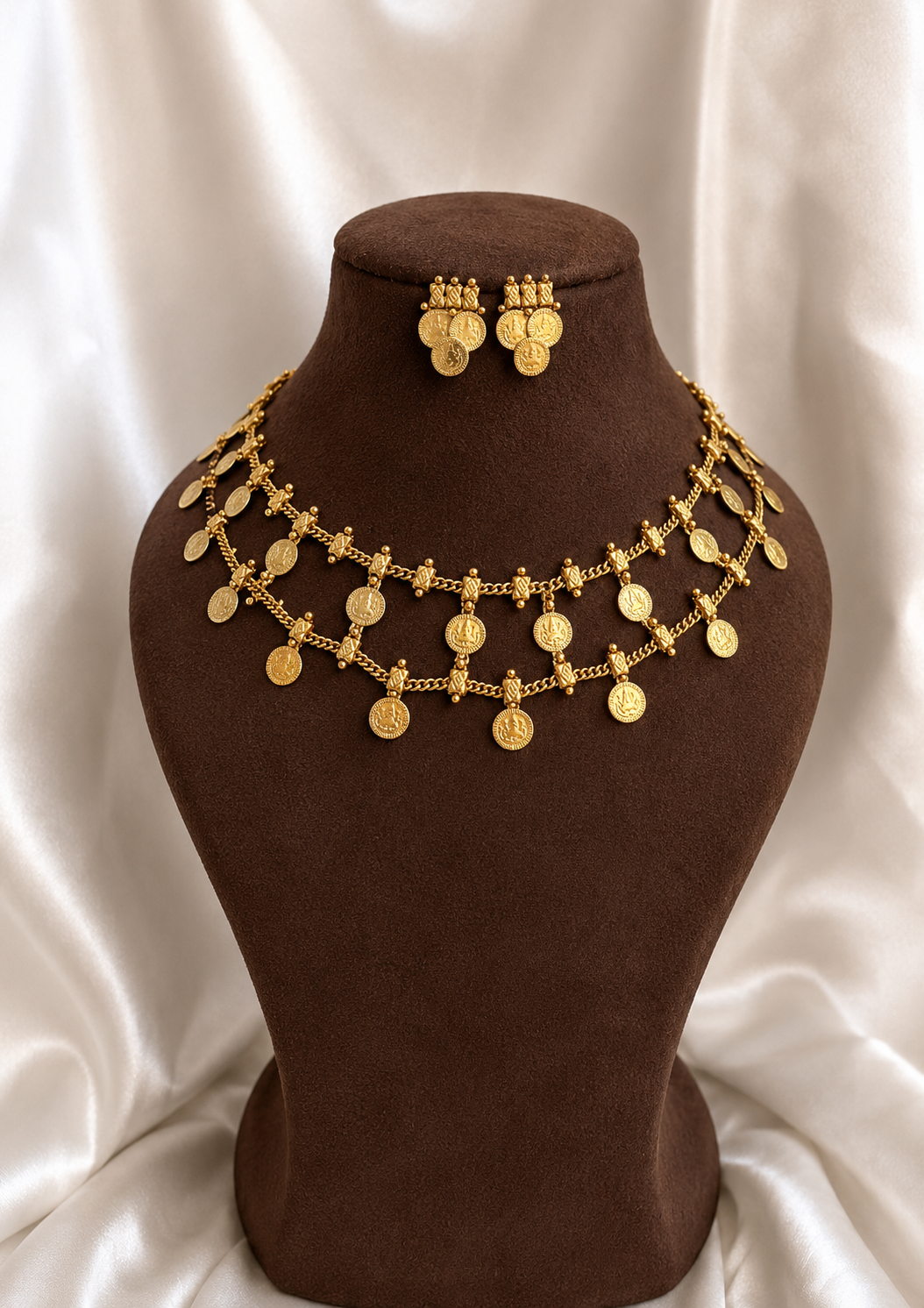 Gold jewelry set consisting of a necklace and matching earrings displayed on a brown velvet bust against a white satin background.