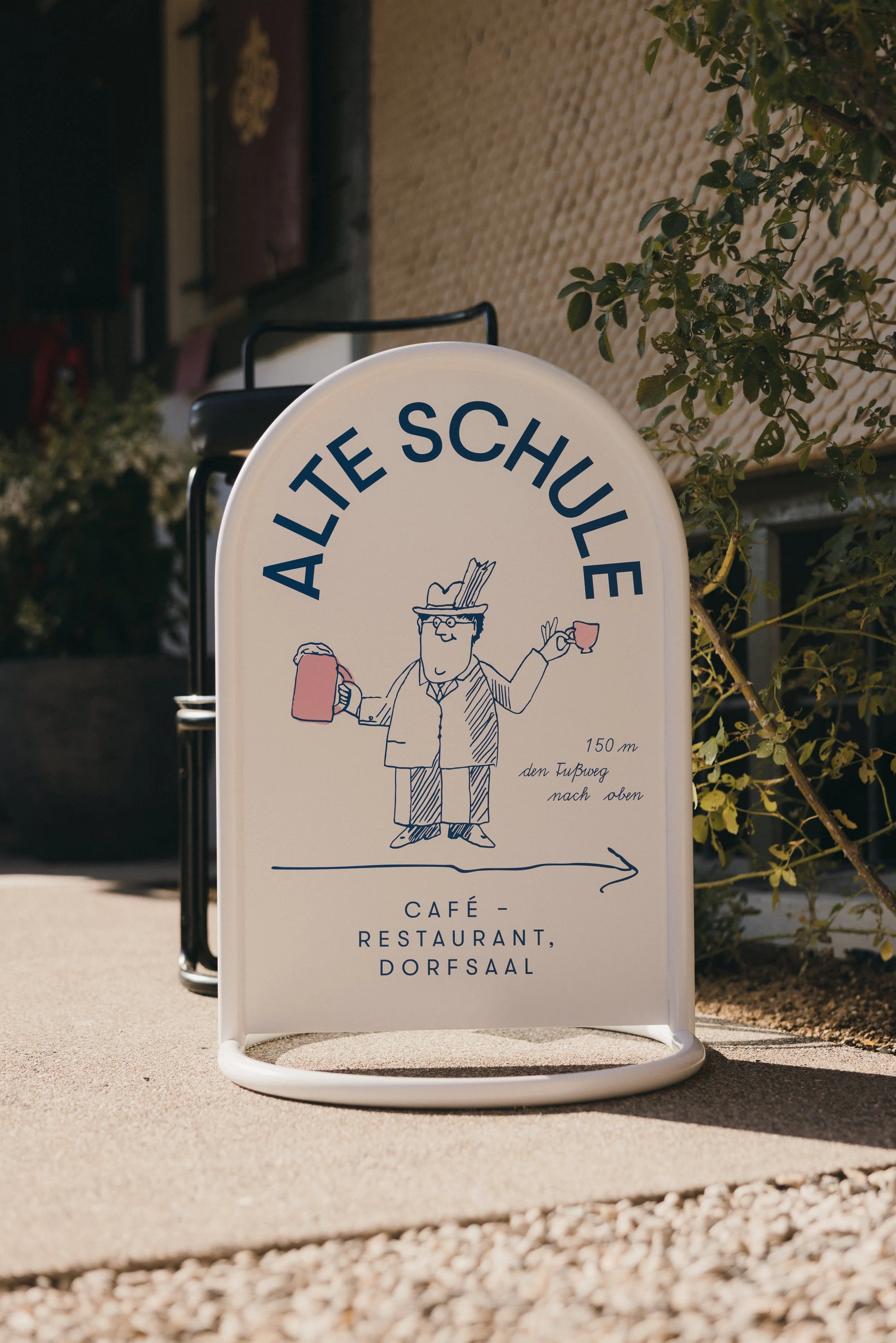Werbeschild für ein Café-Restaurant namens 'Alte Schule', mit einer Illustration eines Mannes, der eine Tasse hält und eine Tüte trägt, mit Text in Deutsch.