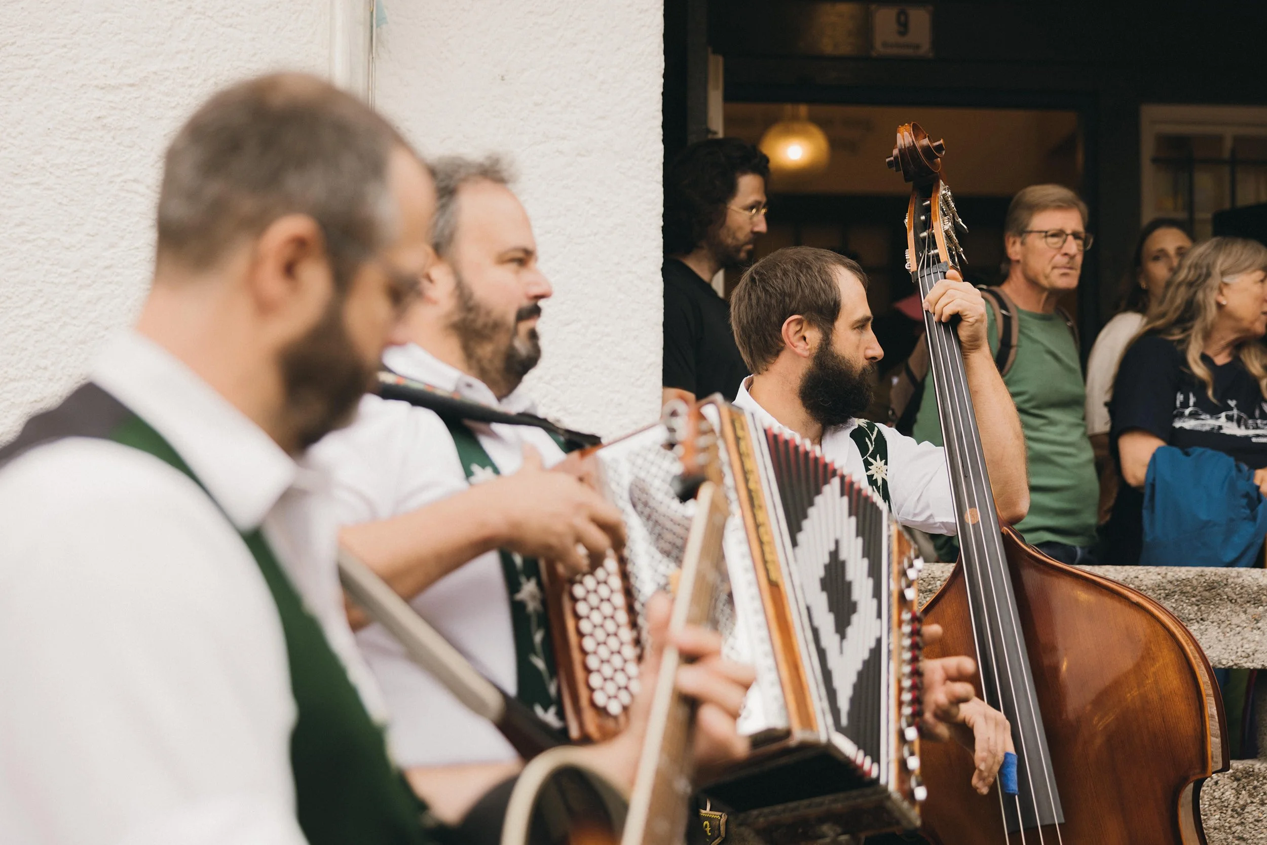 Musiker spielen traditionelle Instrumente während eines Festivals im Freien, mit einer Gruppe von Menschen, die zuschauen, im Hintergrund.