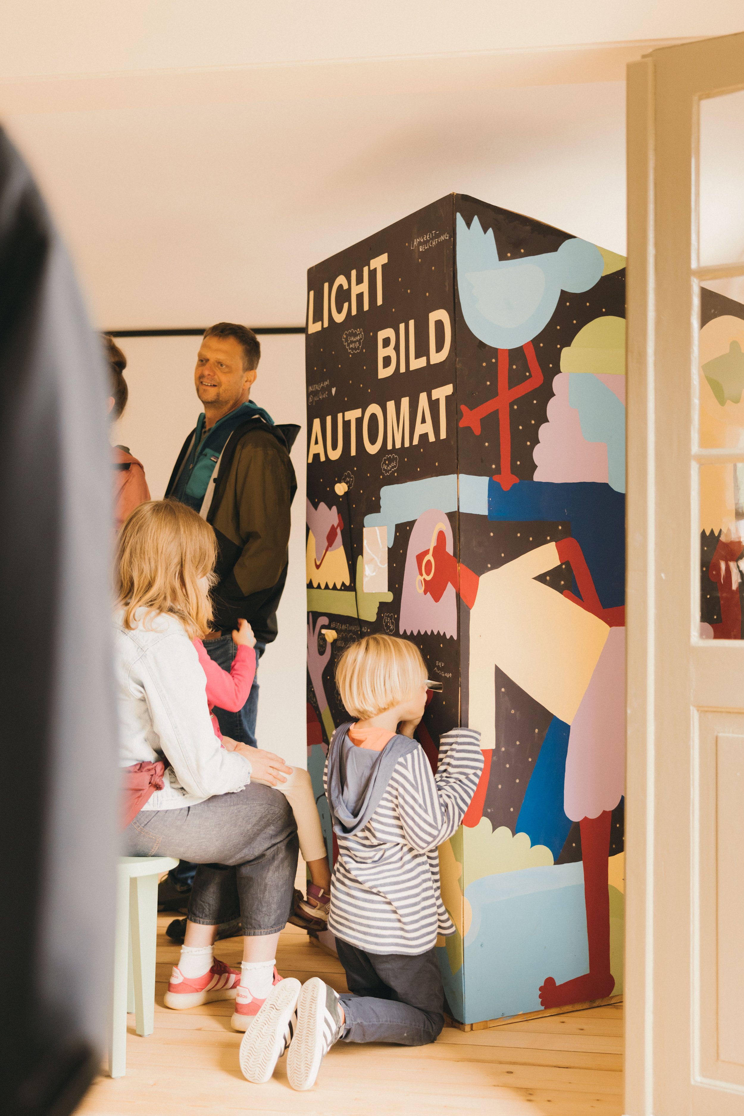 Kinder und Erwachsene vor einem bunten Kunstwerk mit der Aufschrift "Lichtbildautomat".