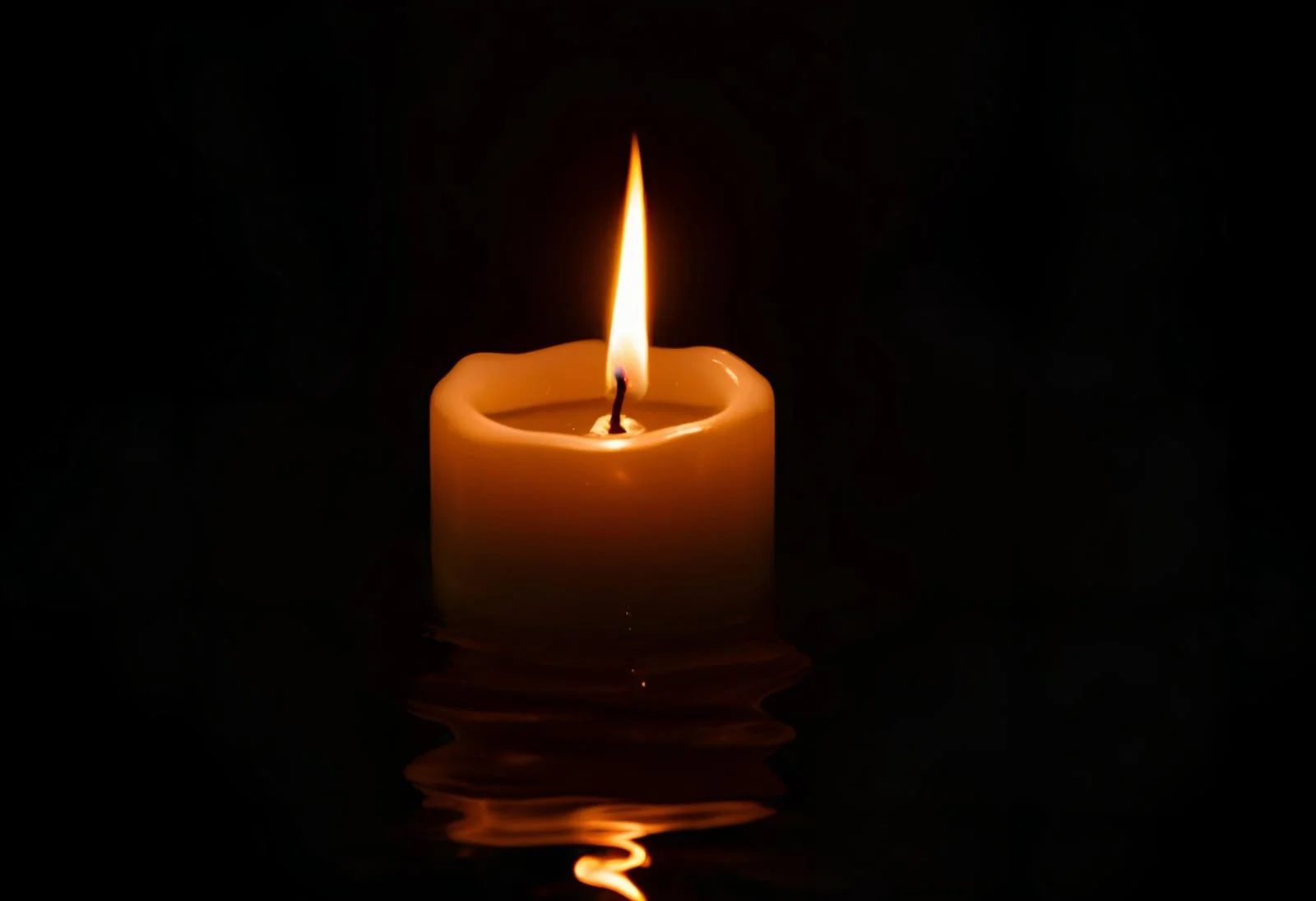 A lit candle floating on dark water with reflections, with a small flame at the top.