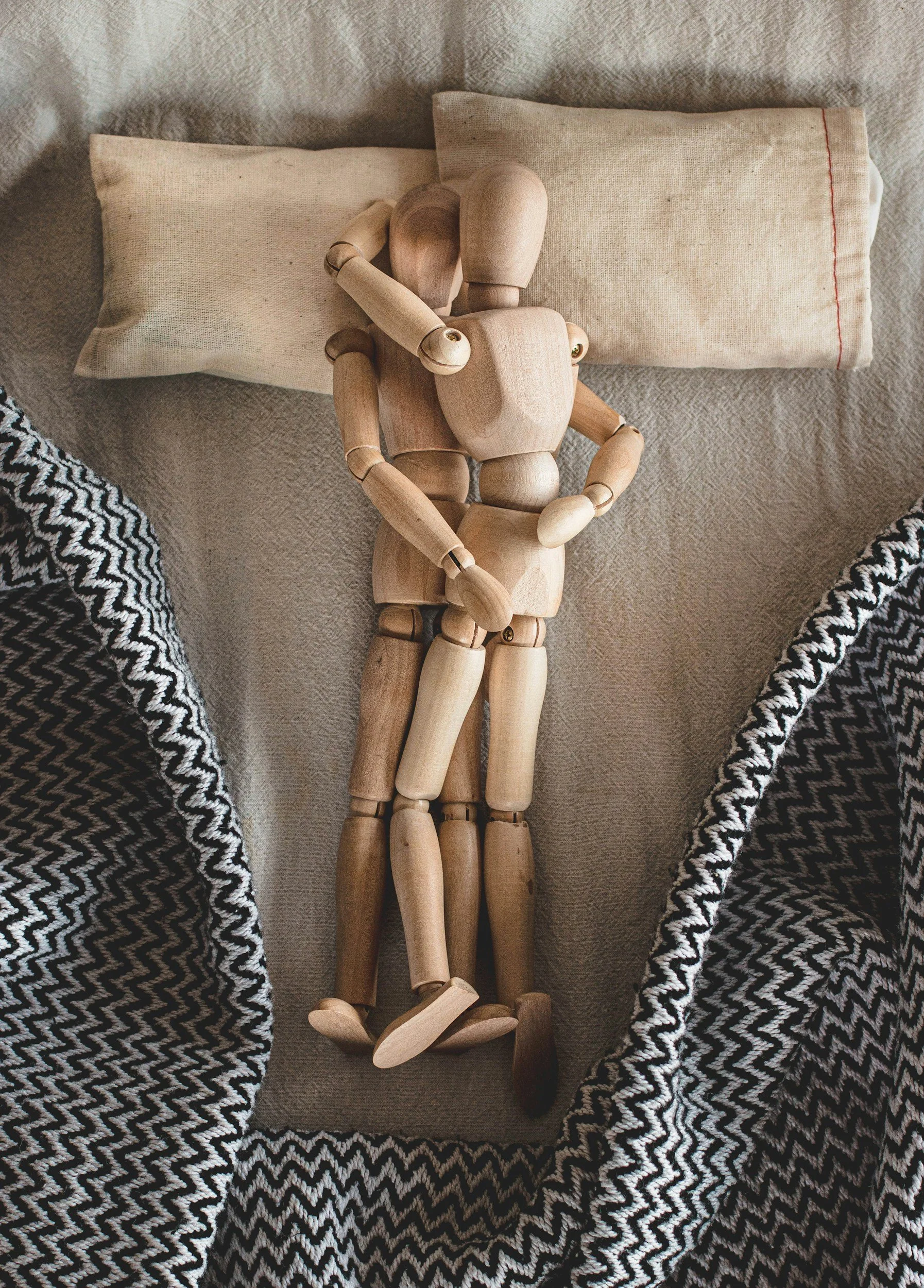 Holz-Puppen, die eine menschliche Figur auf einem Stoffbett darstellt, umgeben von schwarz-weißen Mustertüchern.