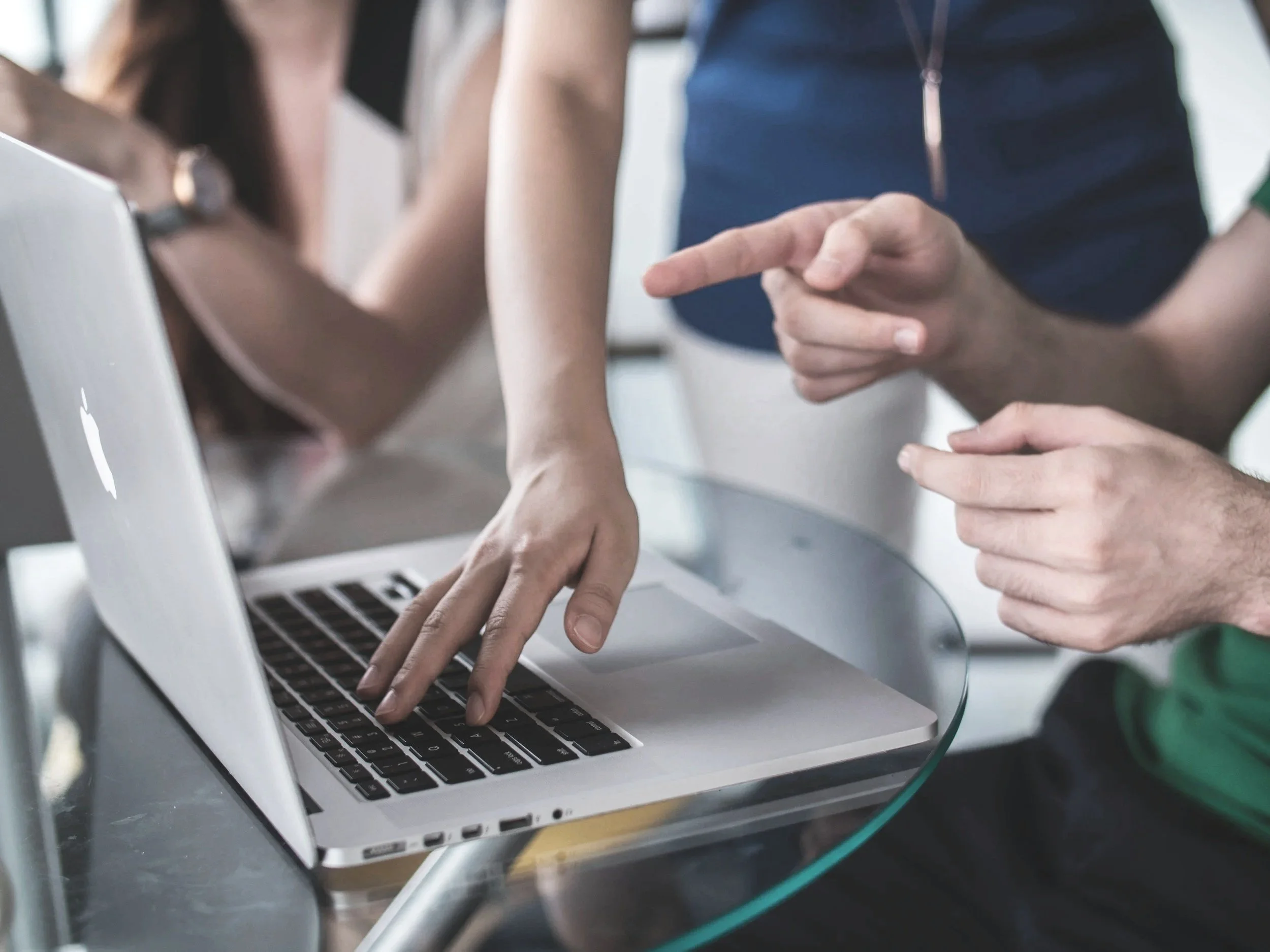 Close-up of two people working together at a laptop, with one person's hand pointing at the keyboard and another person's hand resting on top, in a collaborative setting.