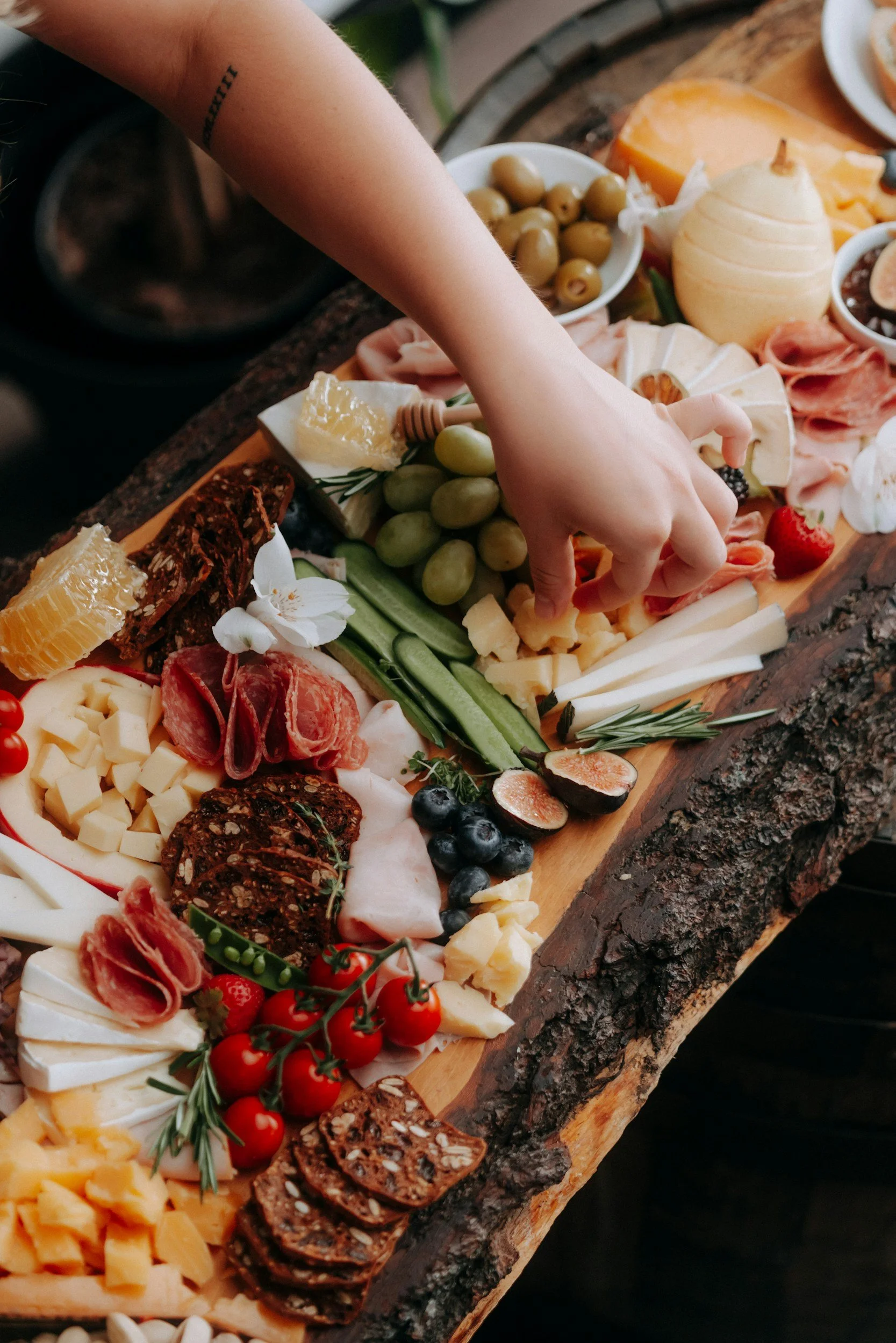 A charcuterie board with various cheeses, meats, fruits, olives, and crackers on a wooden surface.