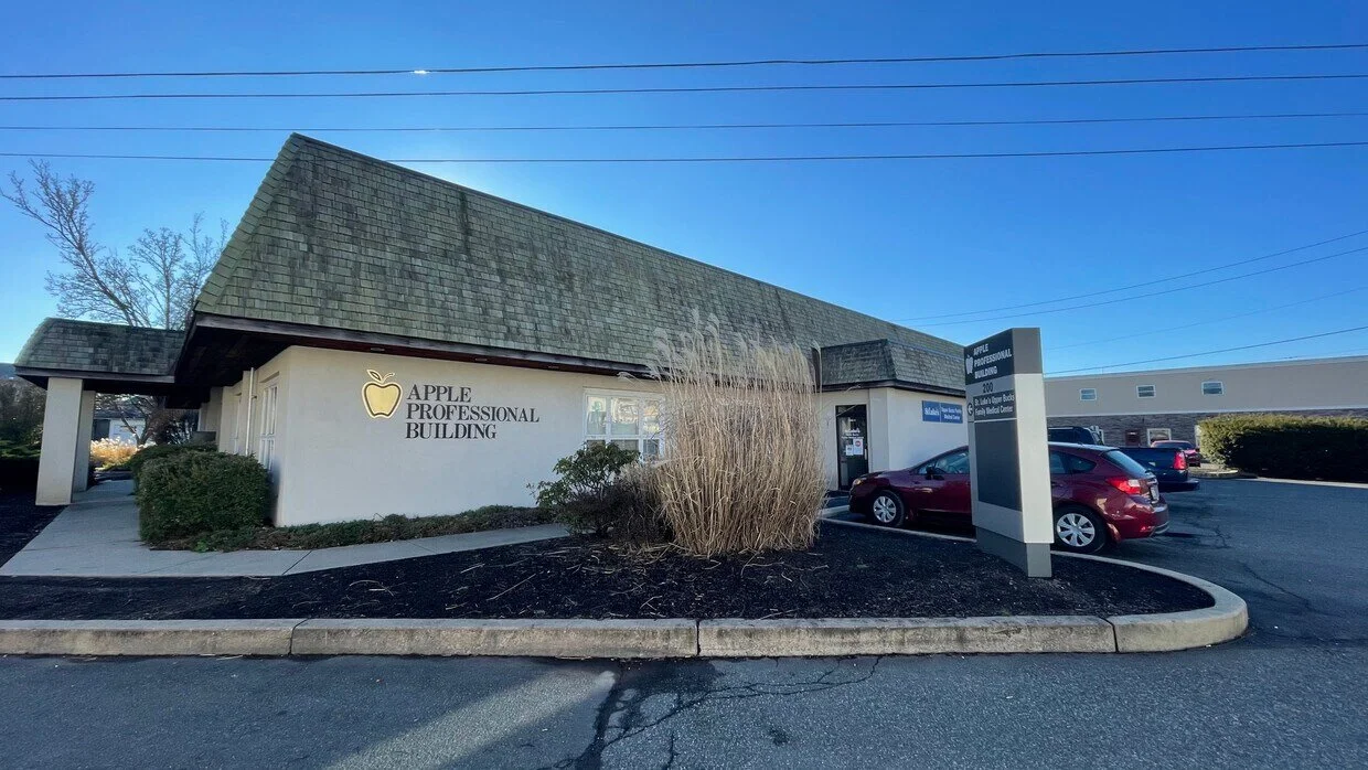 Exterior of a building with a sign reading 'Apple Professional Building', a parking lot with several cars, and clear blue sky.
