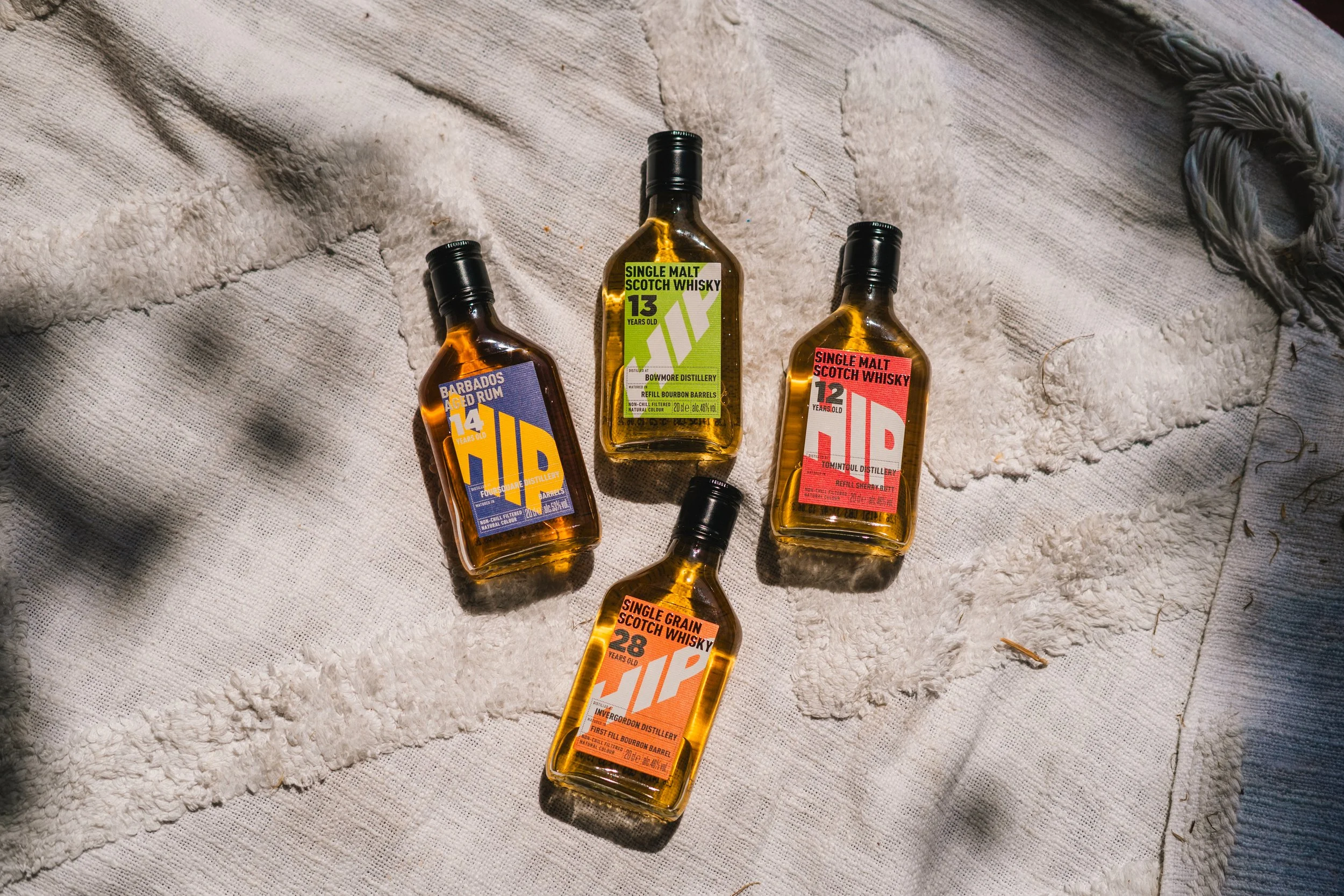 Six bottles of whisky with colorful labels on a textured, off-white fabric surface.