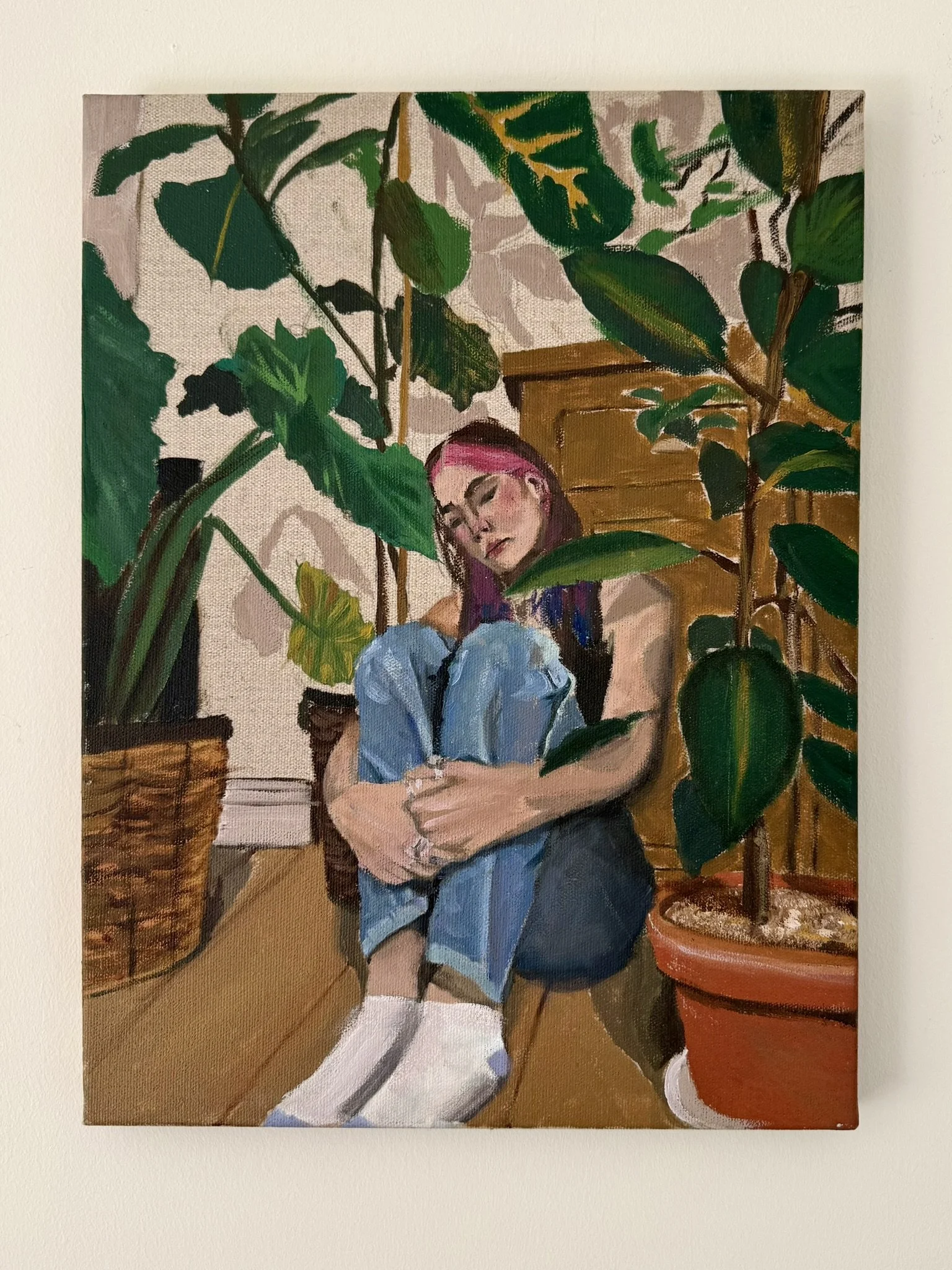 A painting of a young woman with purple hair sitting among large green houseplants, leaning on a piece of furniture, with a wooden dresser in the background.