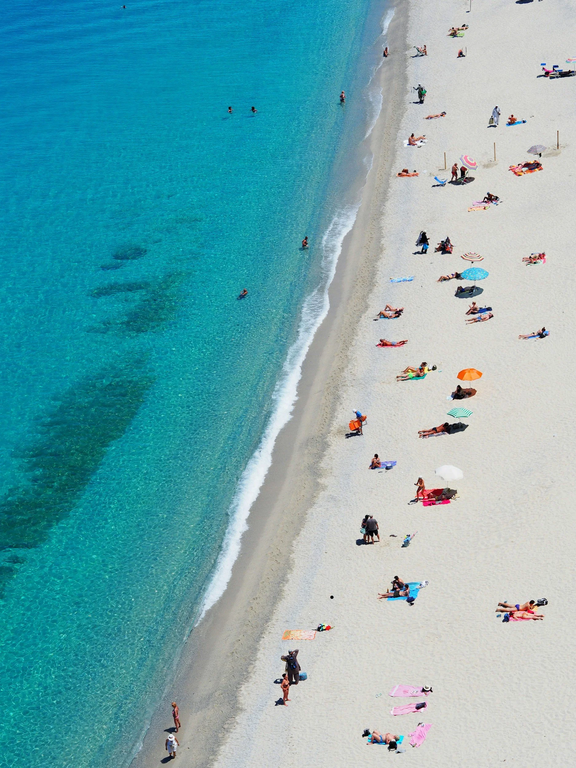 Aerial view of a sandy beach in St. Petersburg, Florida with people sunbathing, walking, and swimming in the turquoise water.