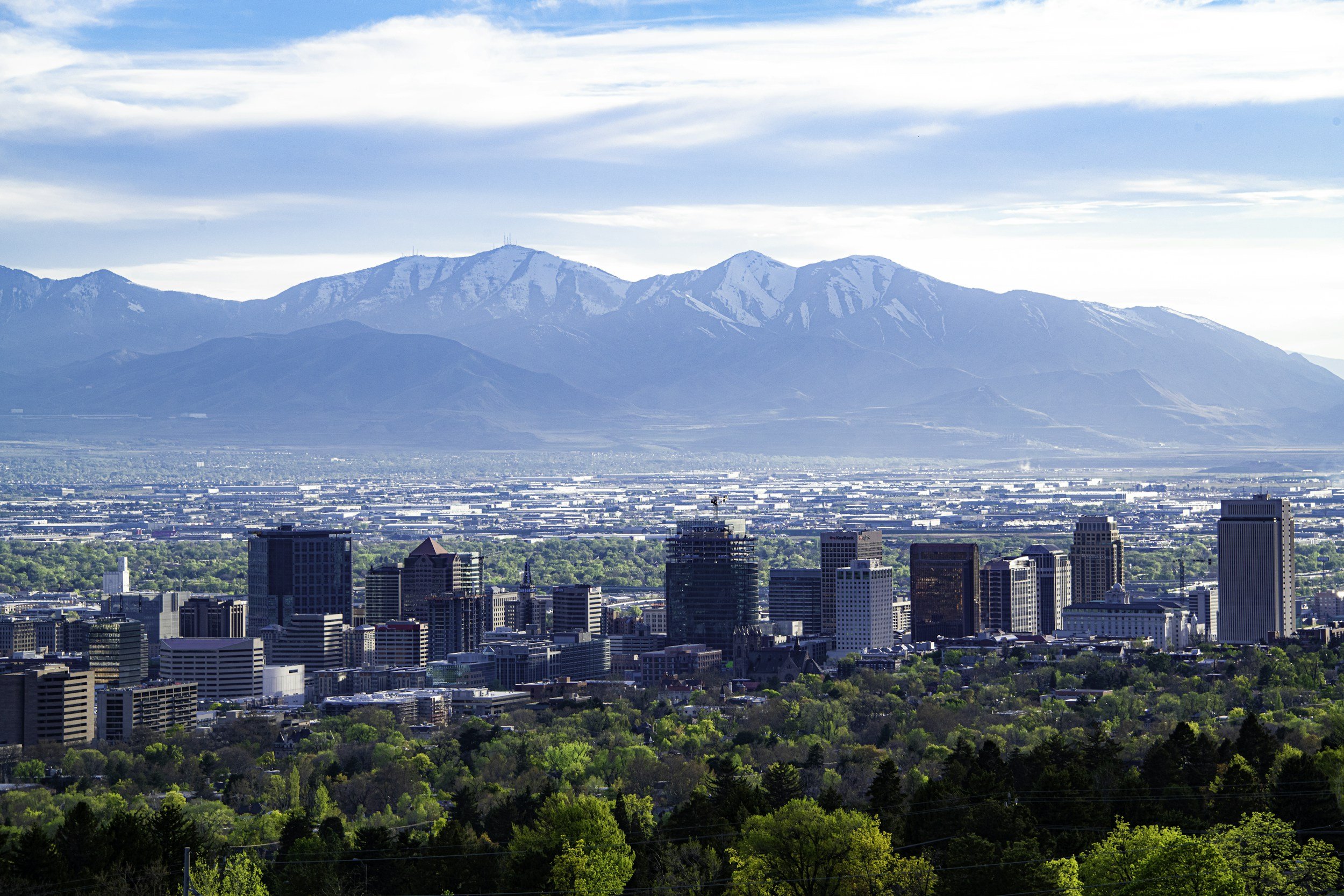 Salt Lake City skyline with a mountain range in the background under a partly cloudy sky.