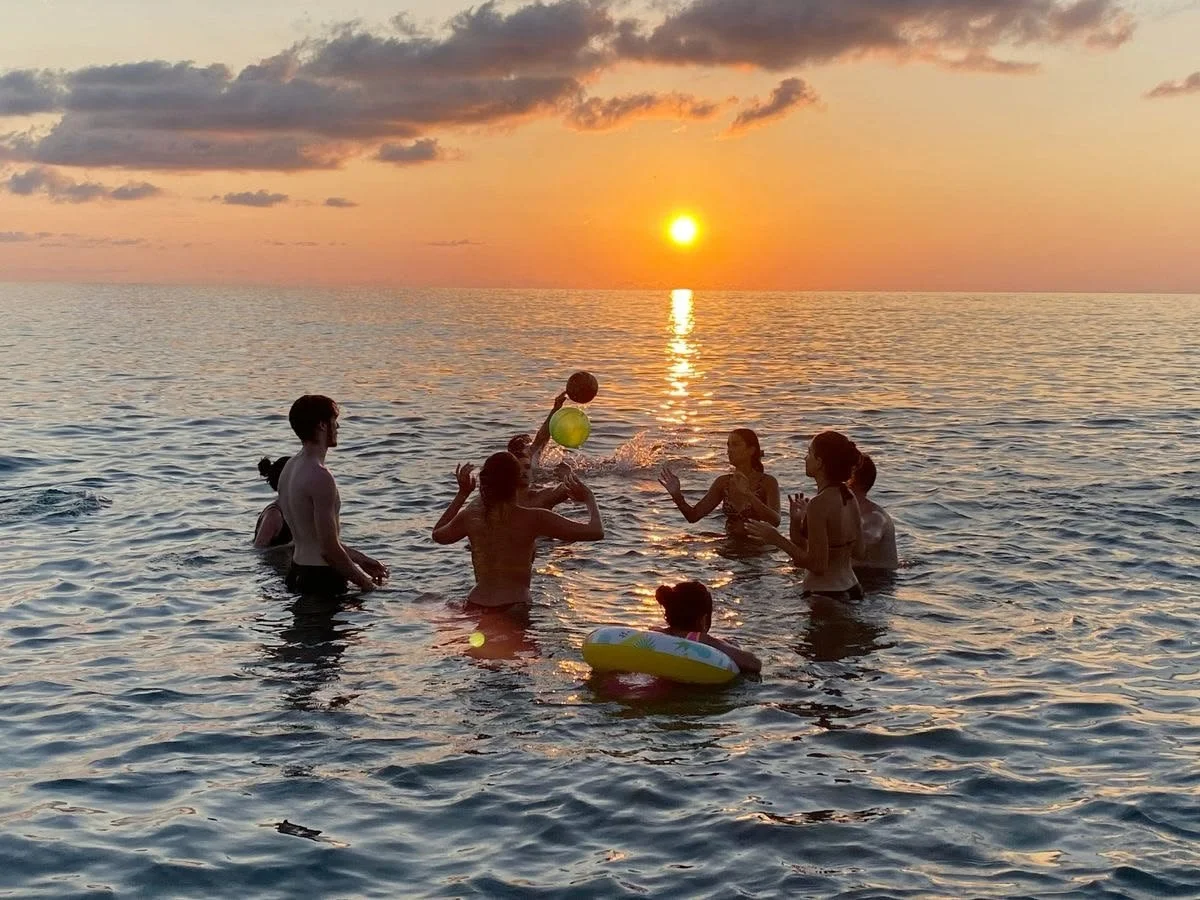 Group of people playing with a ball in the ocean at sunset.
