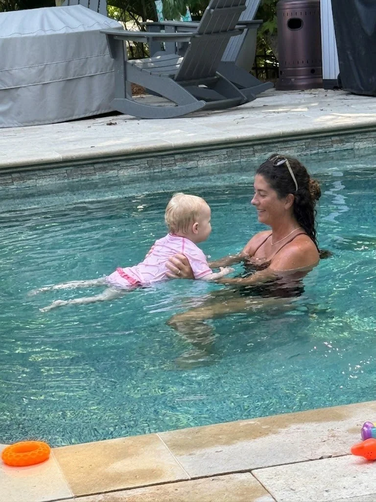 A woman and a young child swimming in a pool, smiling and playing together.