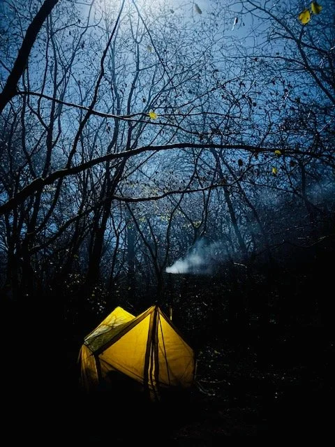 A nightime picture of a small tent with woodburner