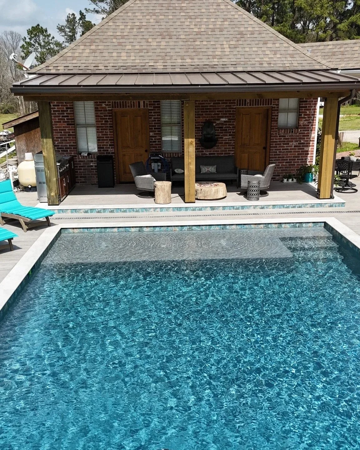 Backyard with a swimming pool, patio furniture, and a brick house with a covered porch.