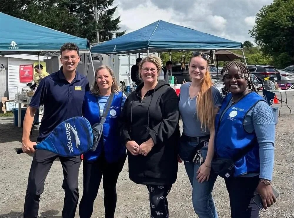 Groupe de bénévoles du Service d'entraide St-Etienne, souriants en extérieur lors d'un événement.