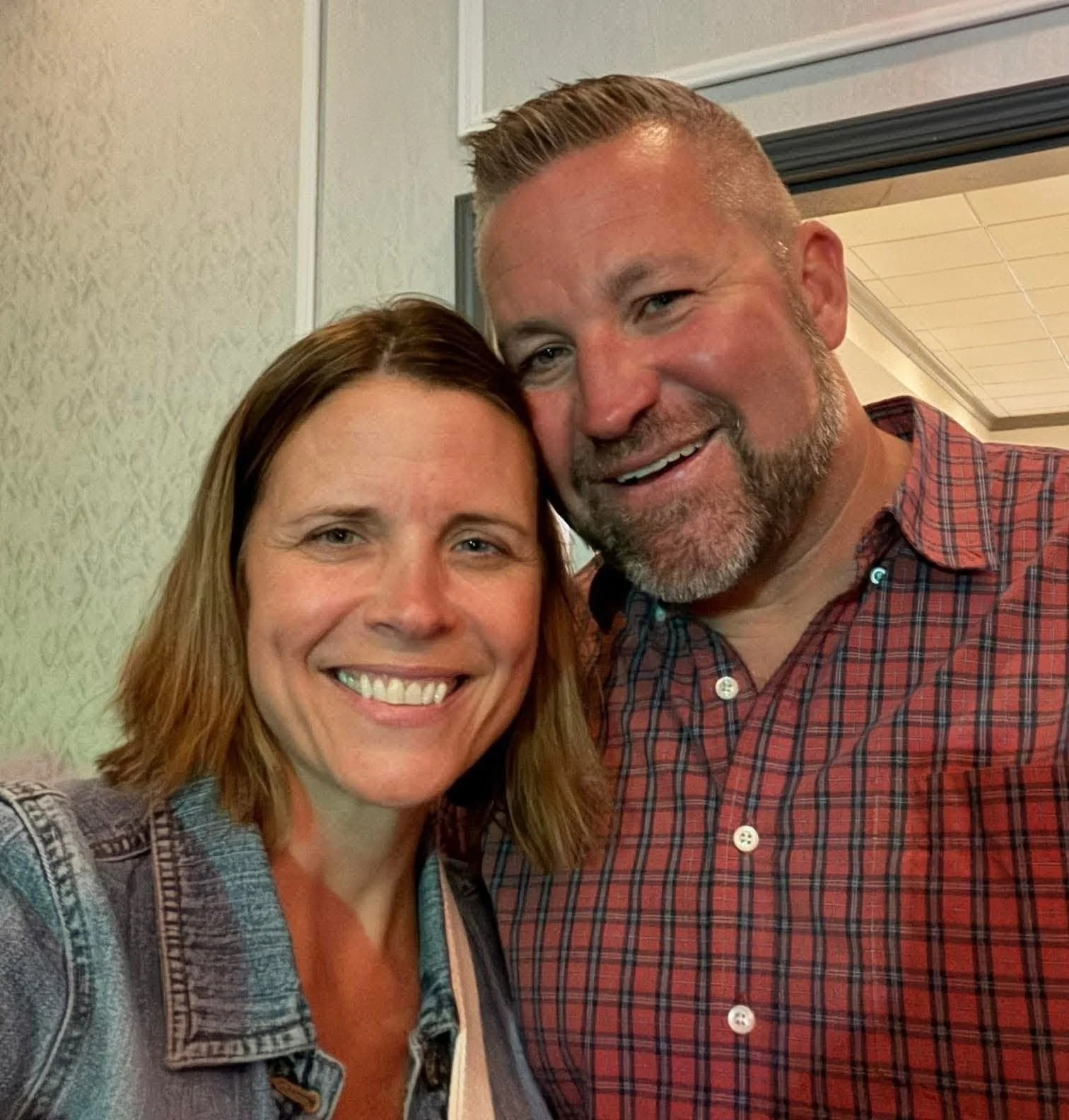 A smiling woman and man taking a selfie together indoors at a social gathering or event.