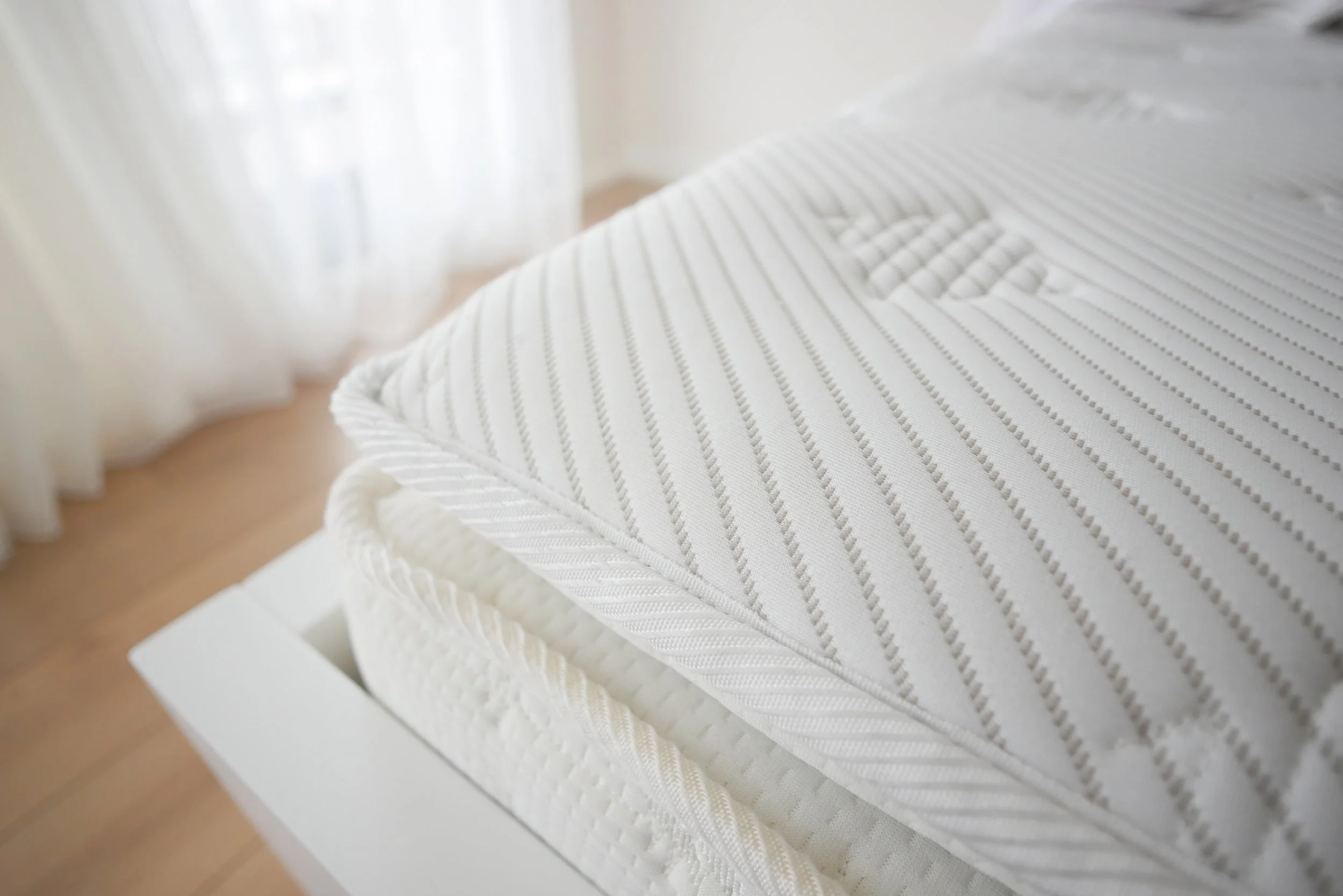 Stacked white pillows with striped and textured patterns on a nightstand next to a bed in a bright room. Safe place to sleep.