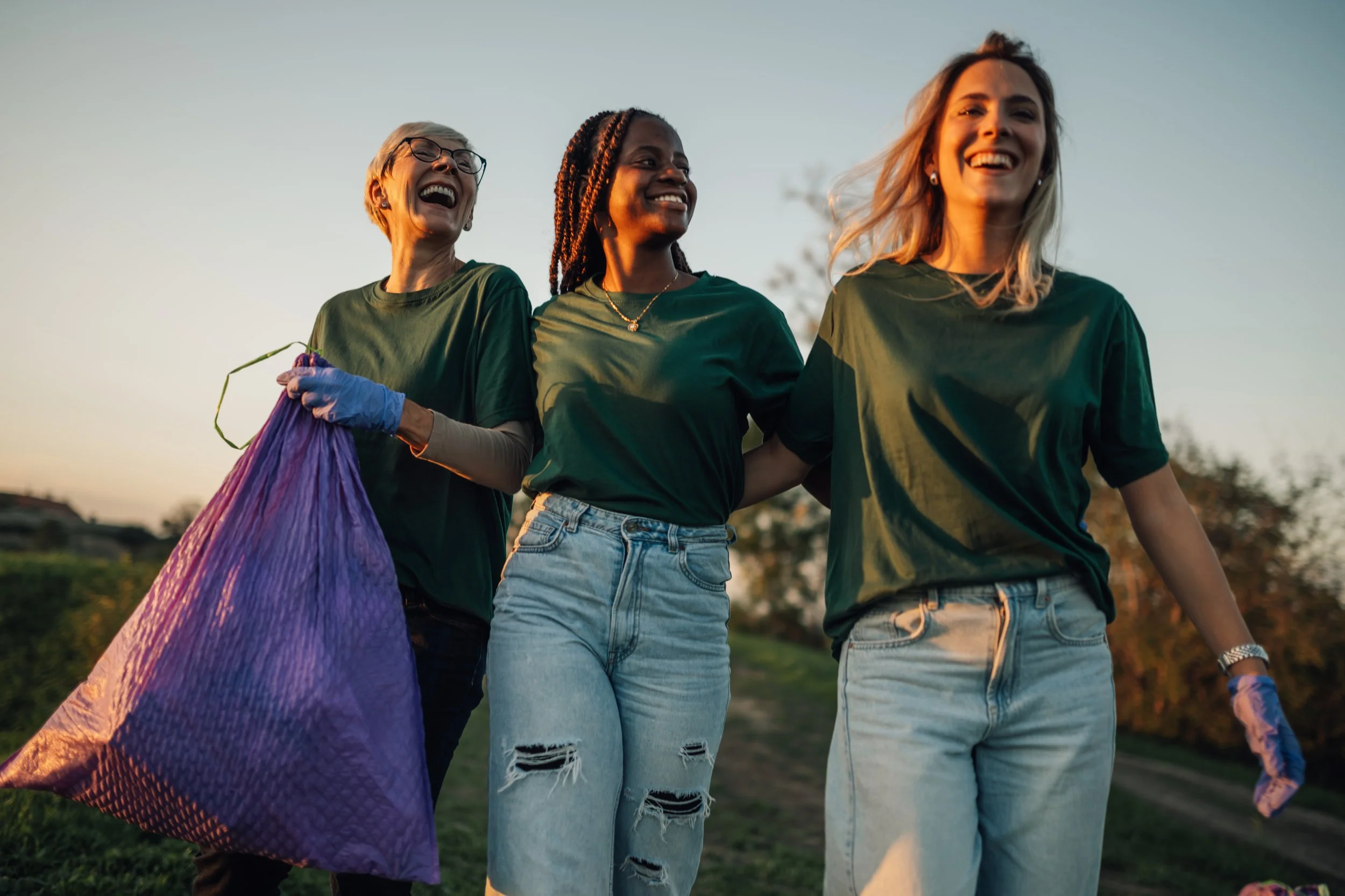 Three women volunteers walking outdoors at sunset, smiling and enjoying each other's company.