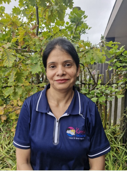Woman with dark hair wearing a navy blue polo shirt standing outdoors in front of greenery and a fence.