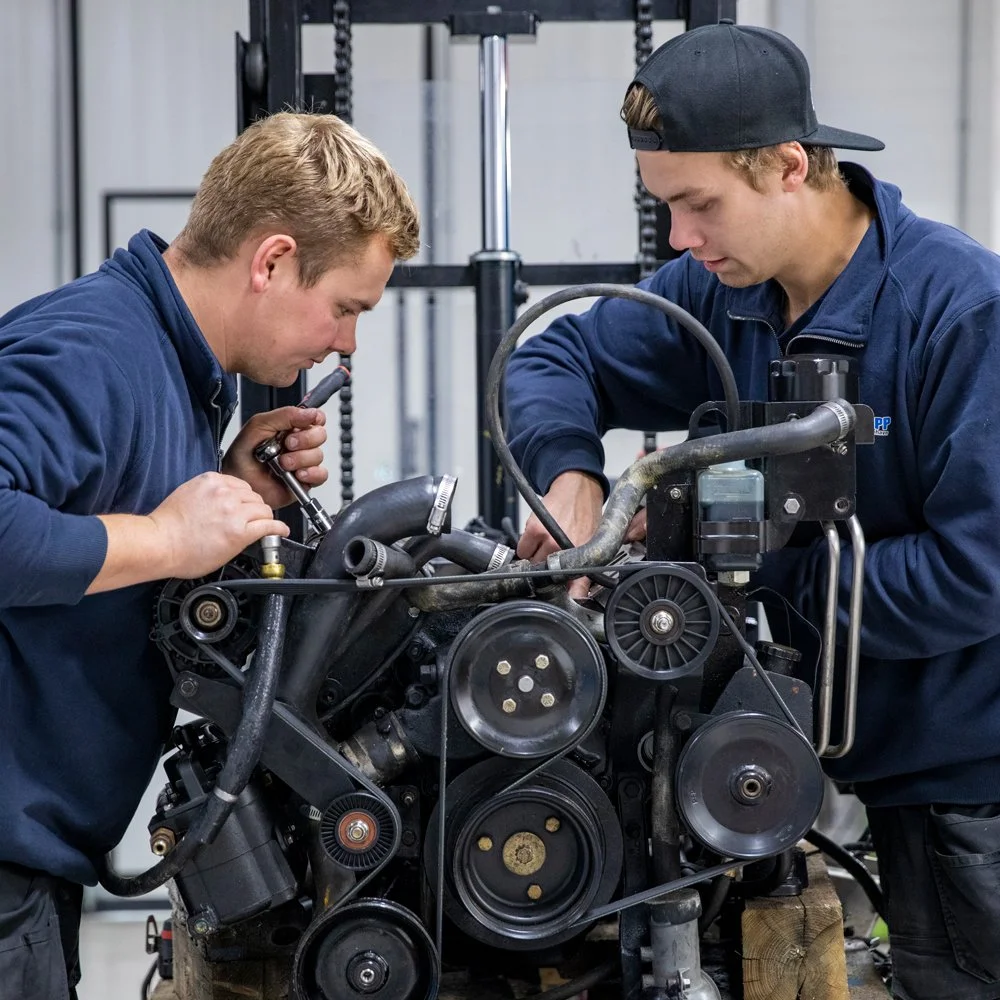 To unge menn som jobber på en motor, plusselige og samarbeider i et verksted.