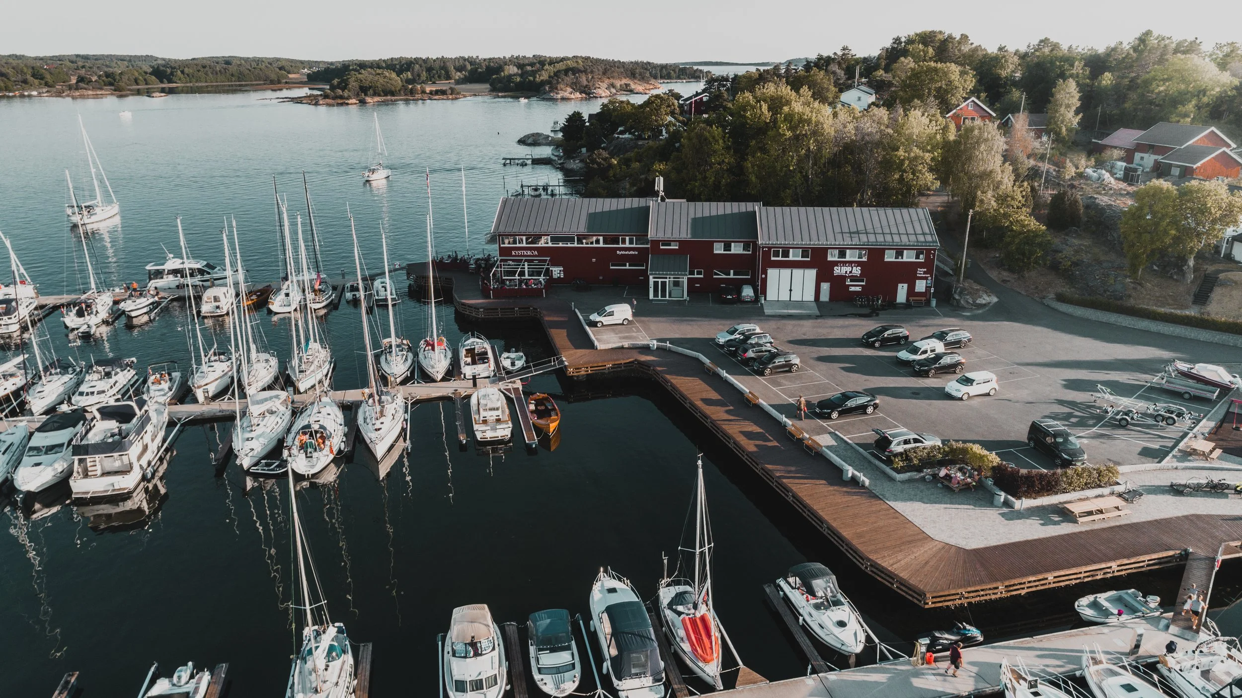 Fler etasjes marina med båter og parkeringsplass omgitt av trær og hus