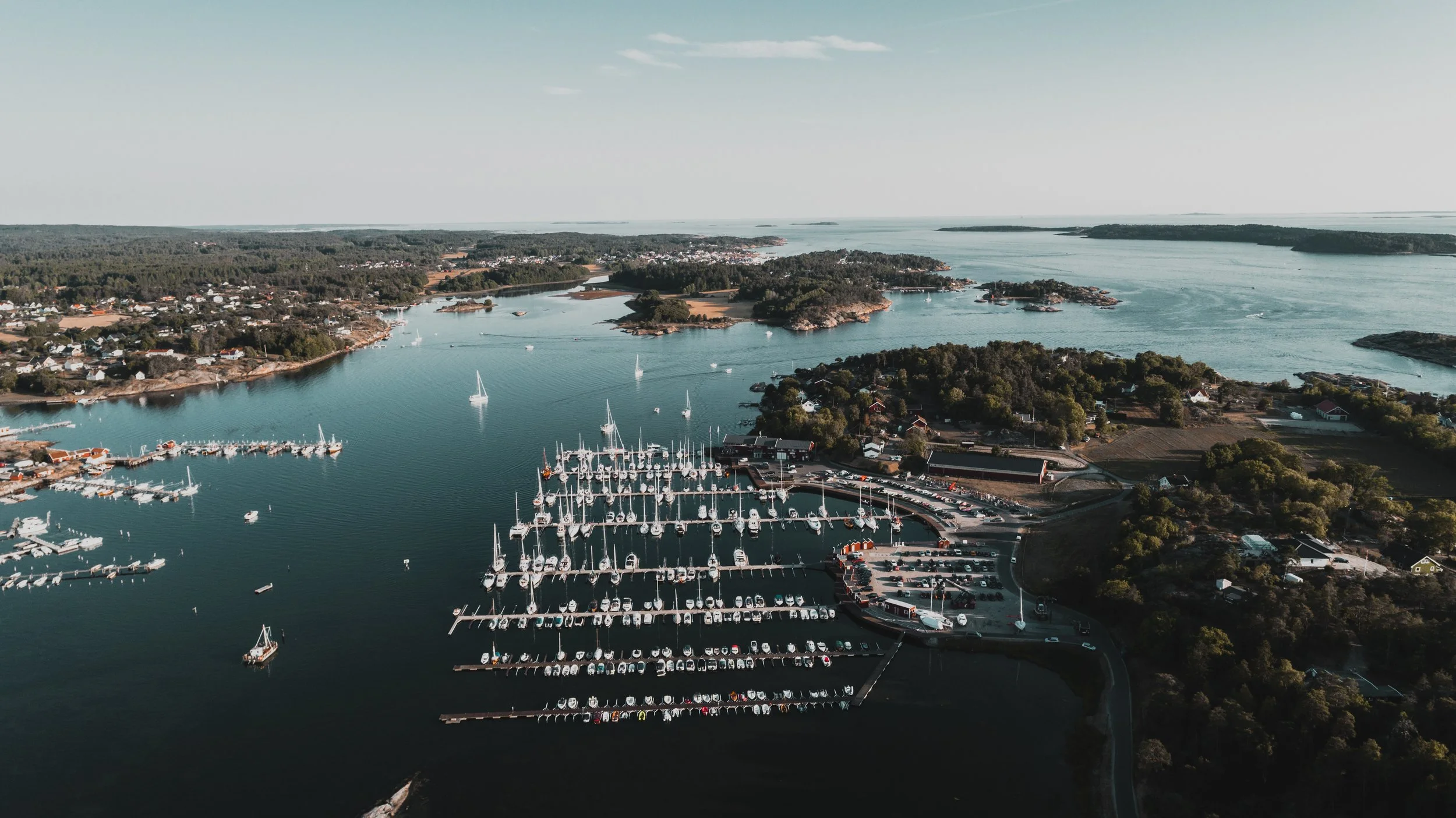 Fjell- og skogkyst med små øyer og en marina med mange båter.