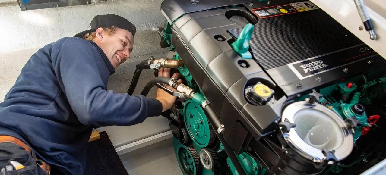 En person som jobber med en bilmotor, som er merket med Volvo Penta, og smiler mens han gjør vedlikehold.
