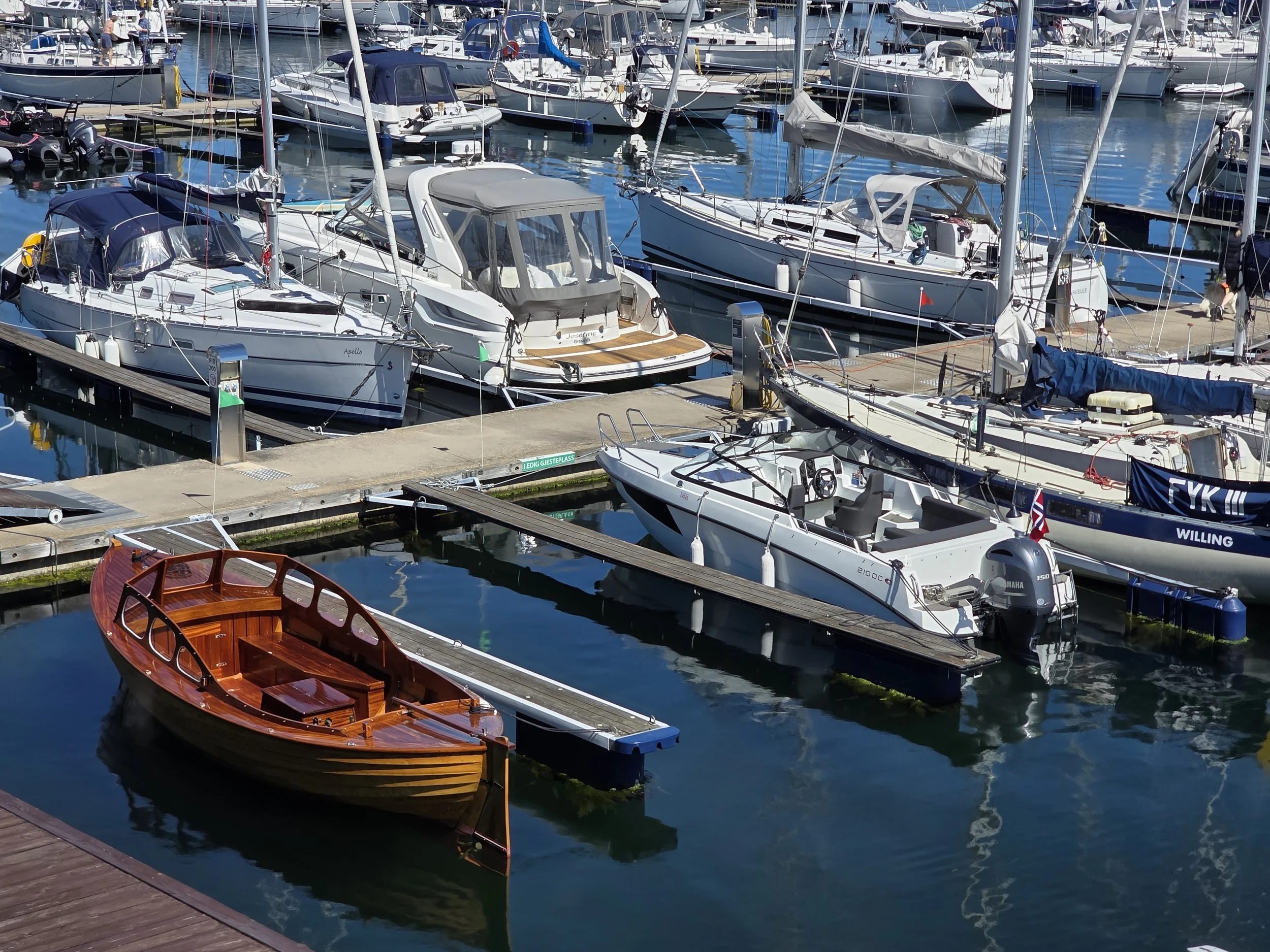 Fargede båter i en brygge ved vannet, mange seilbåter og motorbåter inntil hverandre.