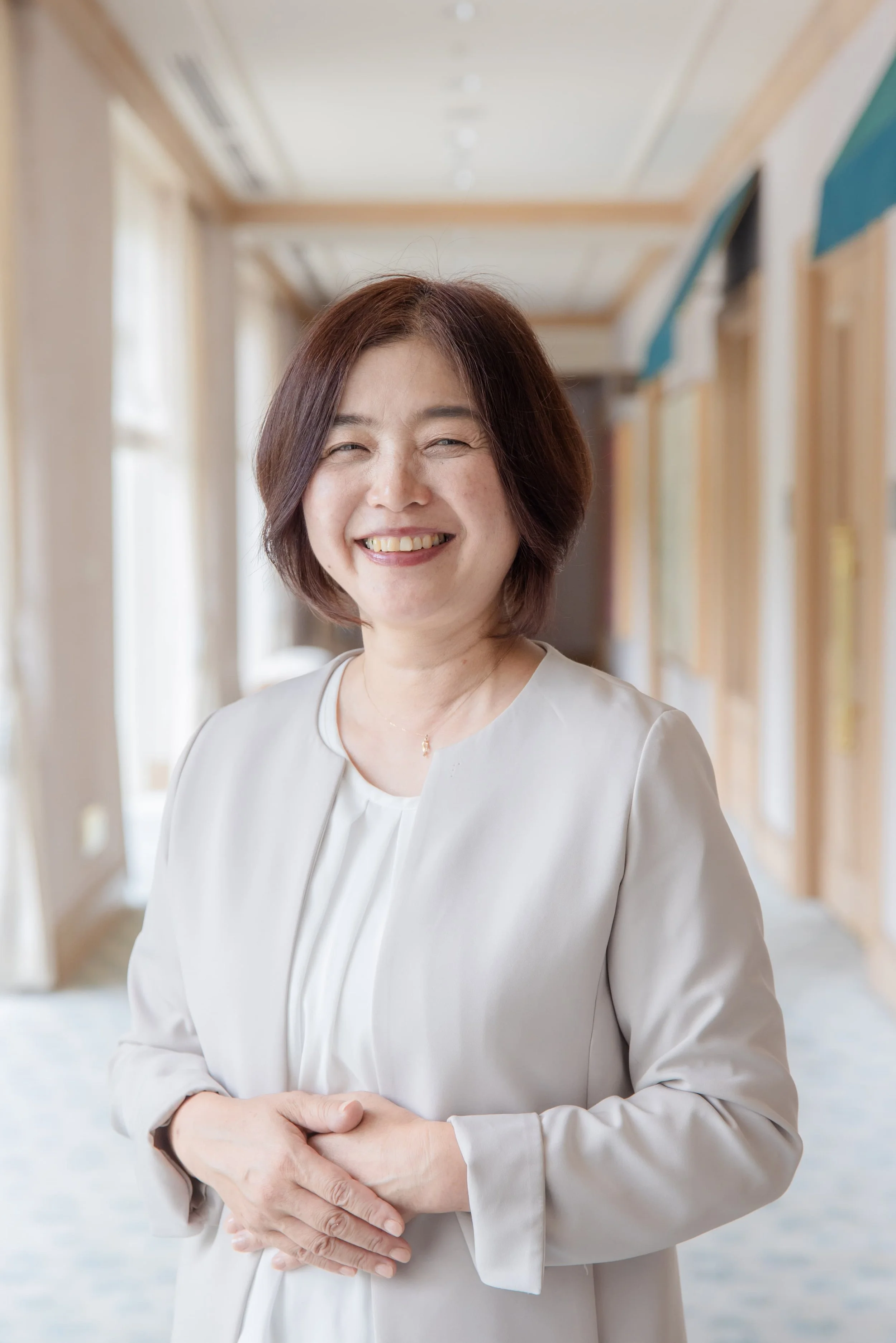 白い服を着た笑顔の女性が屋内の廊下に立っている。