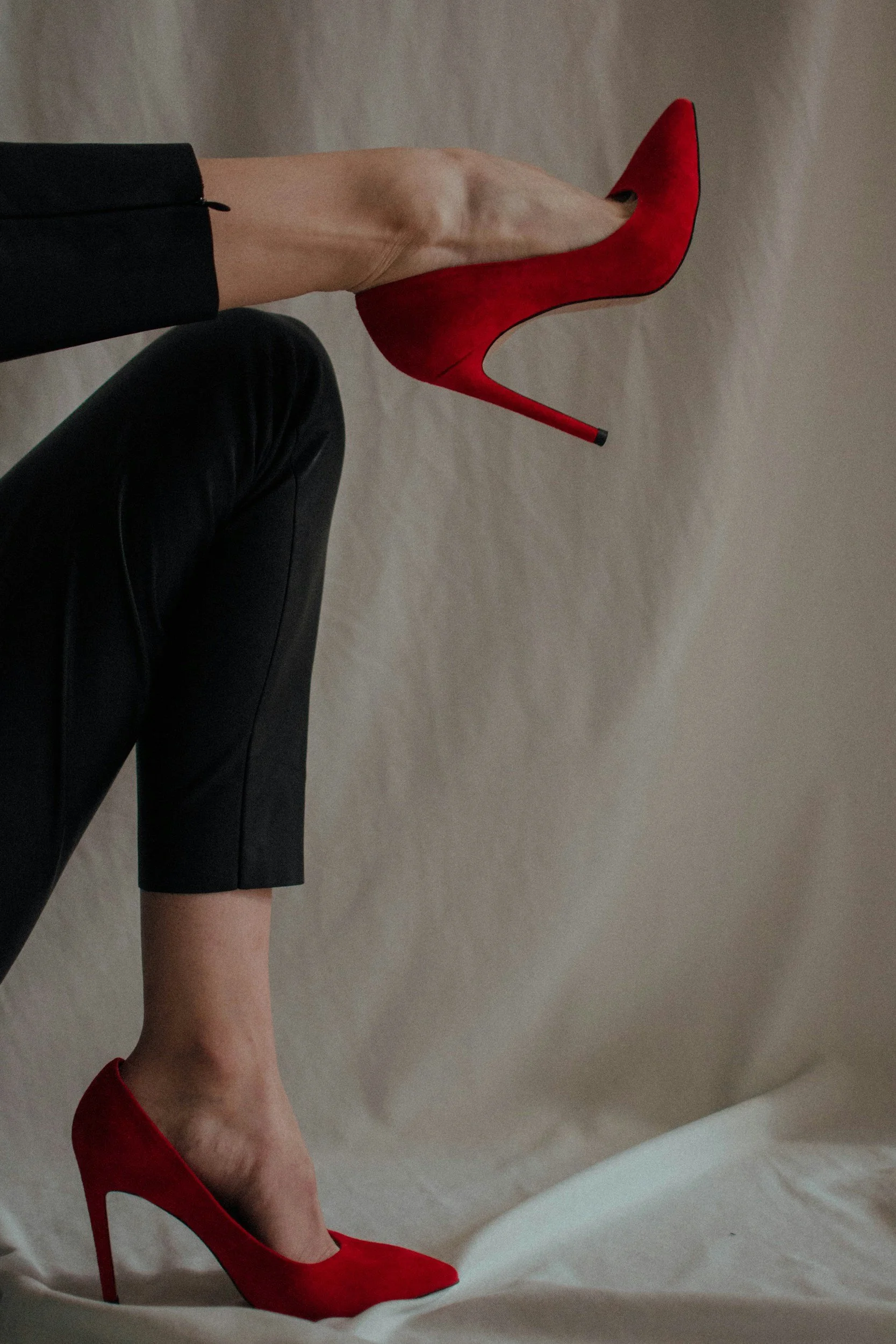A person wearing black pants and red high heels standing on a white surface with a white background.