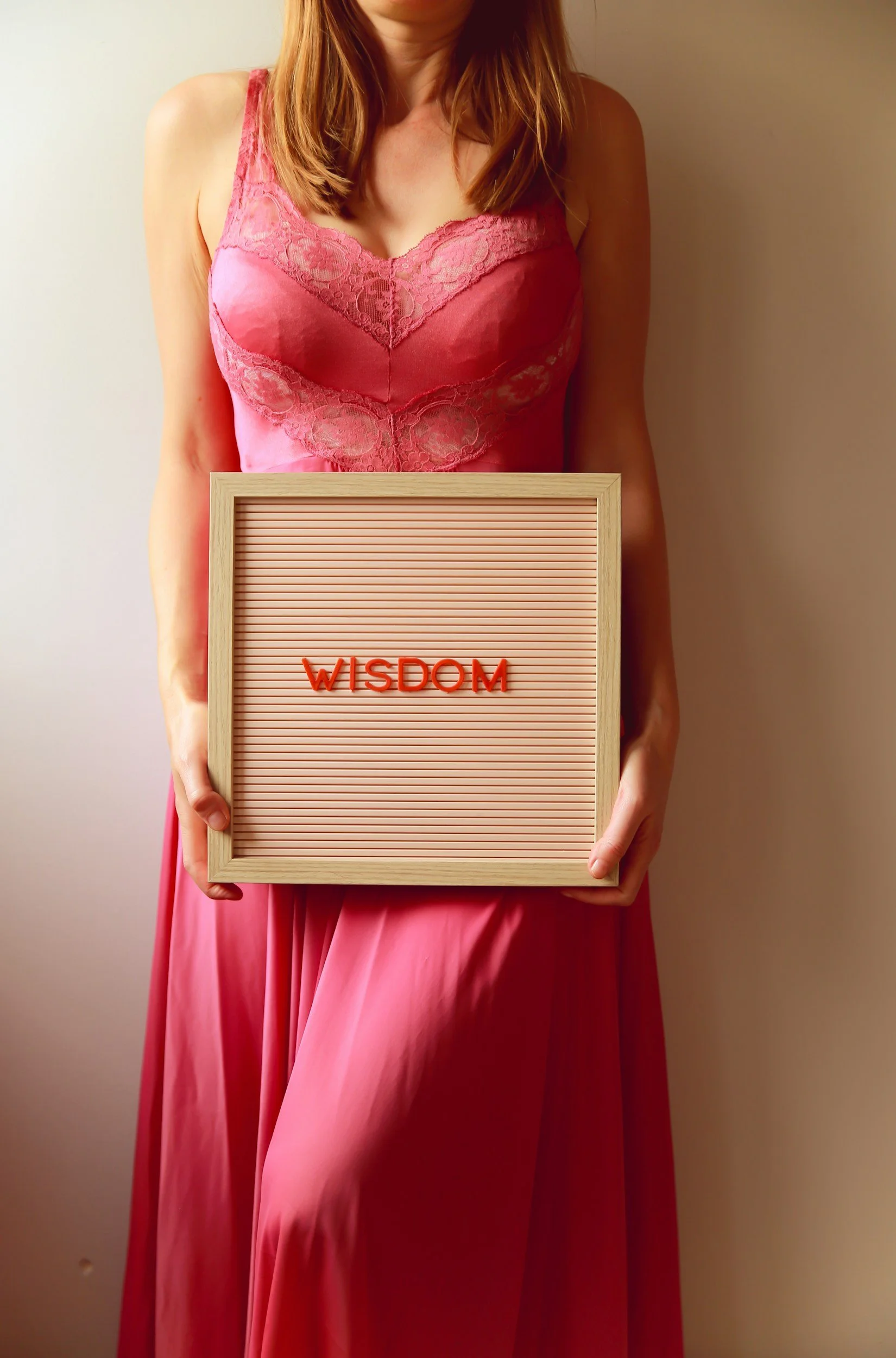 A woman in a pink dress holding a letter board with the word 'WISDOM' written on it.