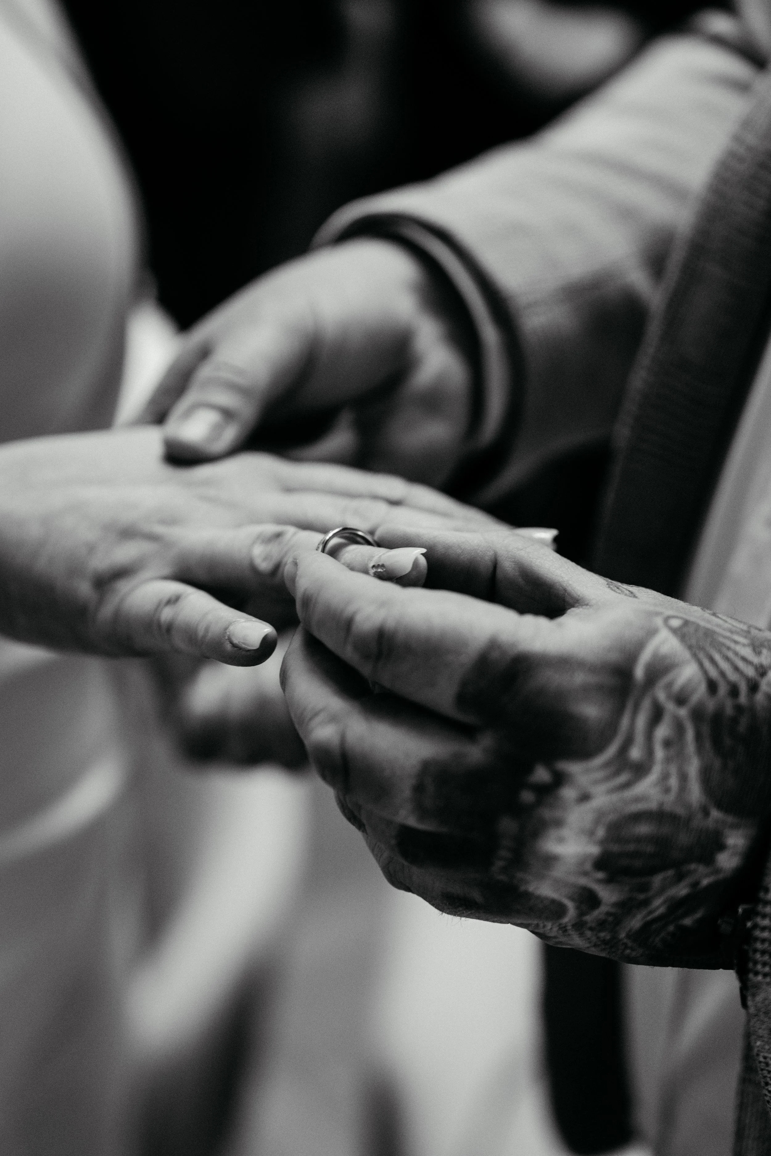 Nahaufnahme von zwei Händen, die sich berühren, eine Hand trägt einen Ehering, die Szene ist in Schwarz-Weiß fotografiert.