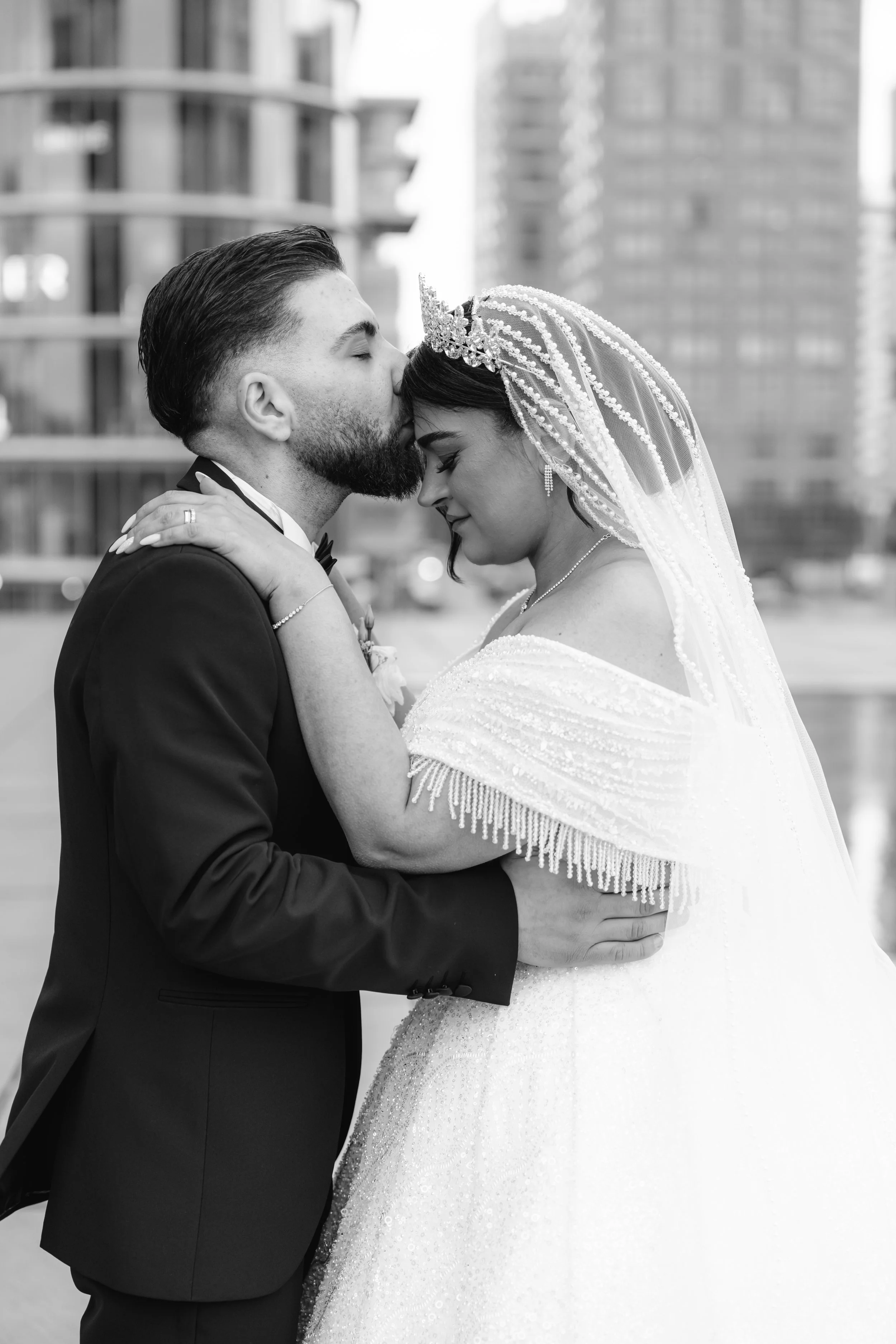 Ein Mann und eine Frau in Hochzeitskleidung umarmen sich in einer urbanen Umgebung.