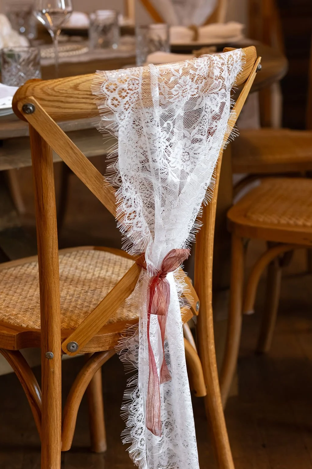 A wooden chair decorated with a piece of white lace fabric tied with a pink ribbon, set in a rustic dining area.