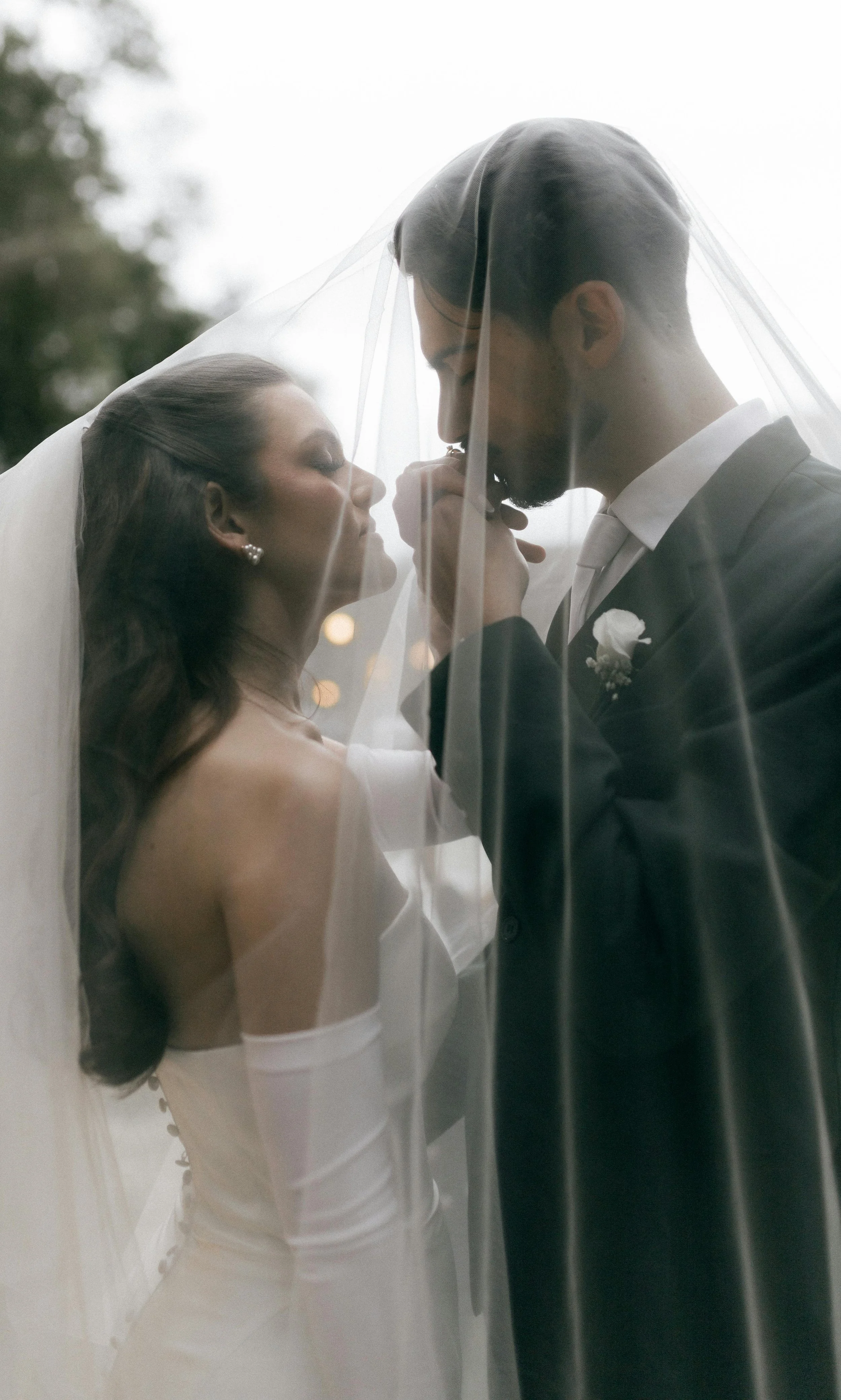 A bride and groom standing close together with a wedding veil draped over both of them, sharing an intimate moment during their wedding.