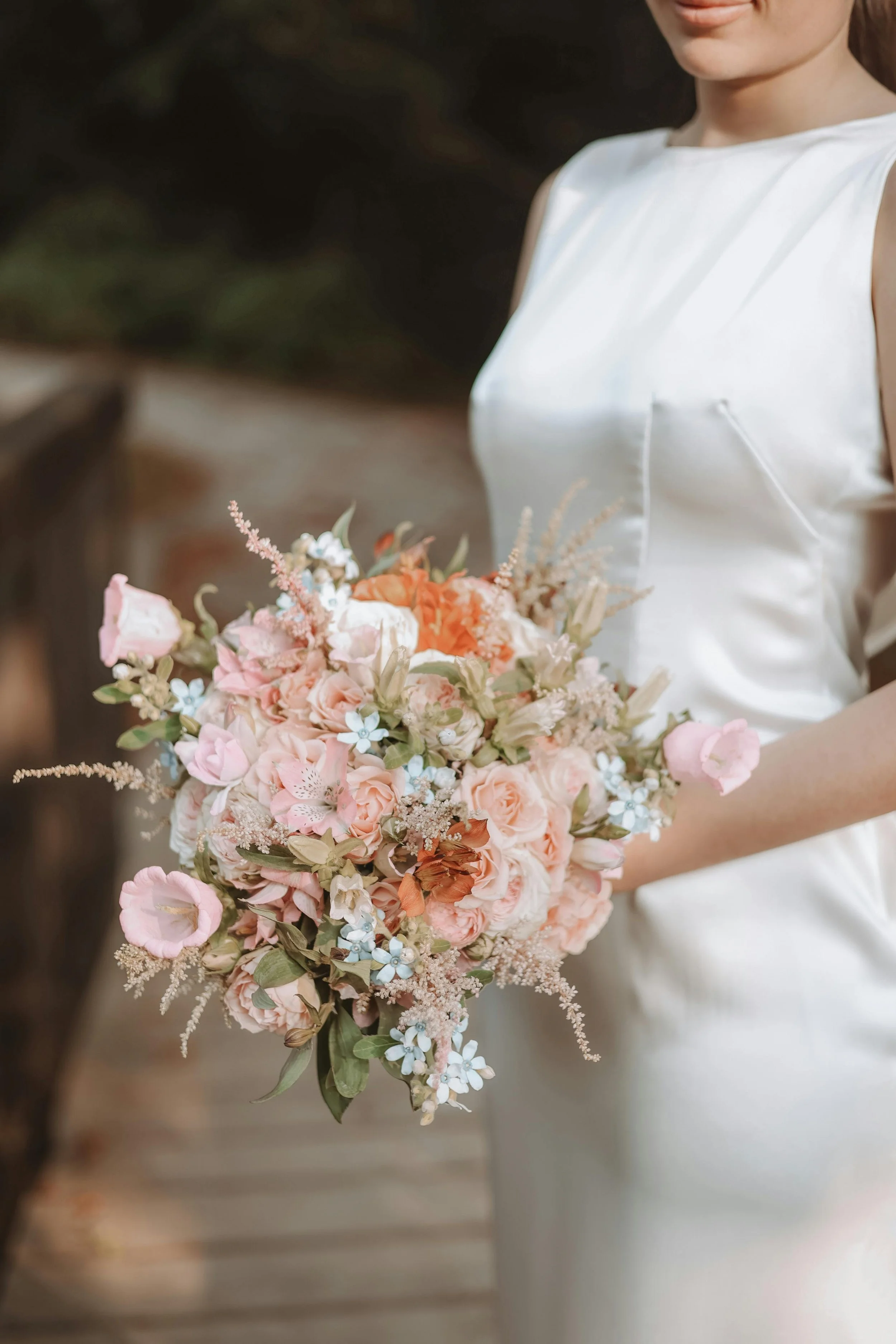 A woman in a white dress holding a large bouquet of pink, white, and peach flowers.
